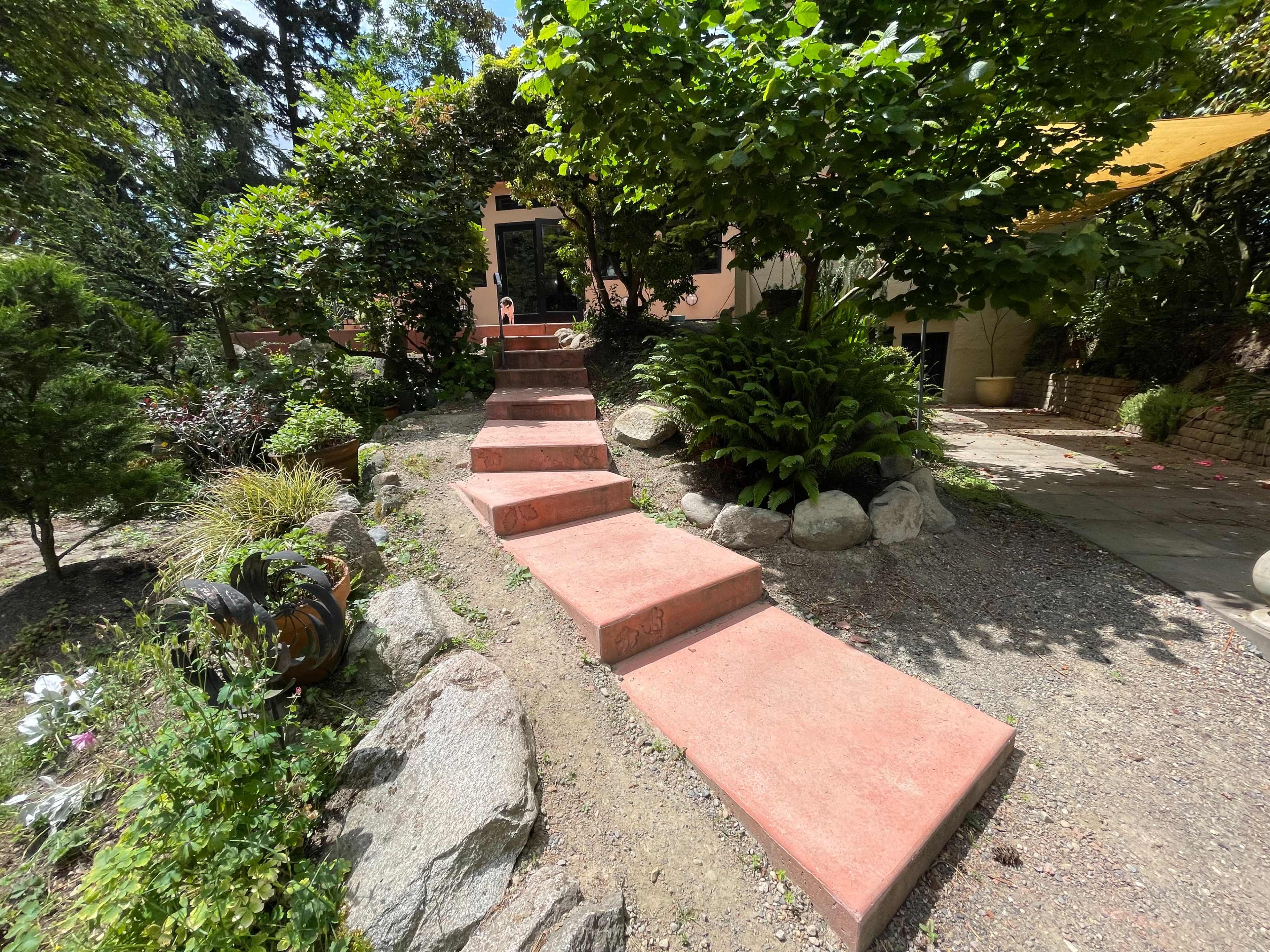 A set of stone steps leads from a garden path up to a house, surrounded by greenery and decorative elements.