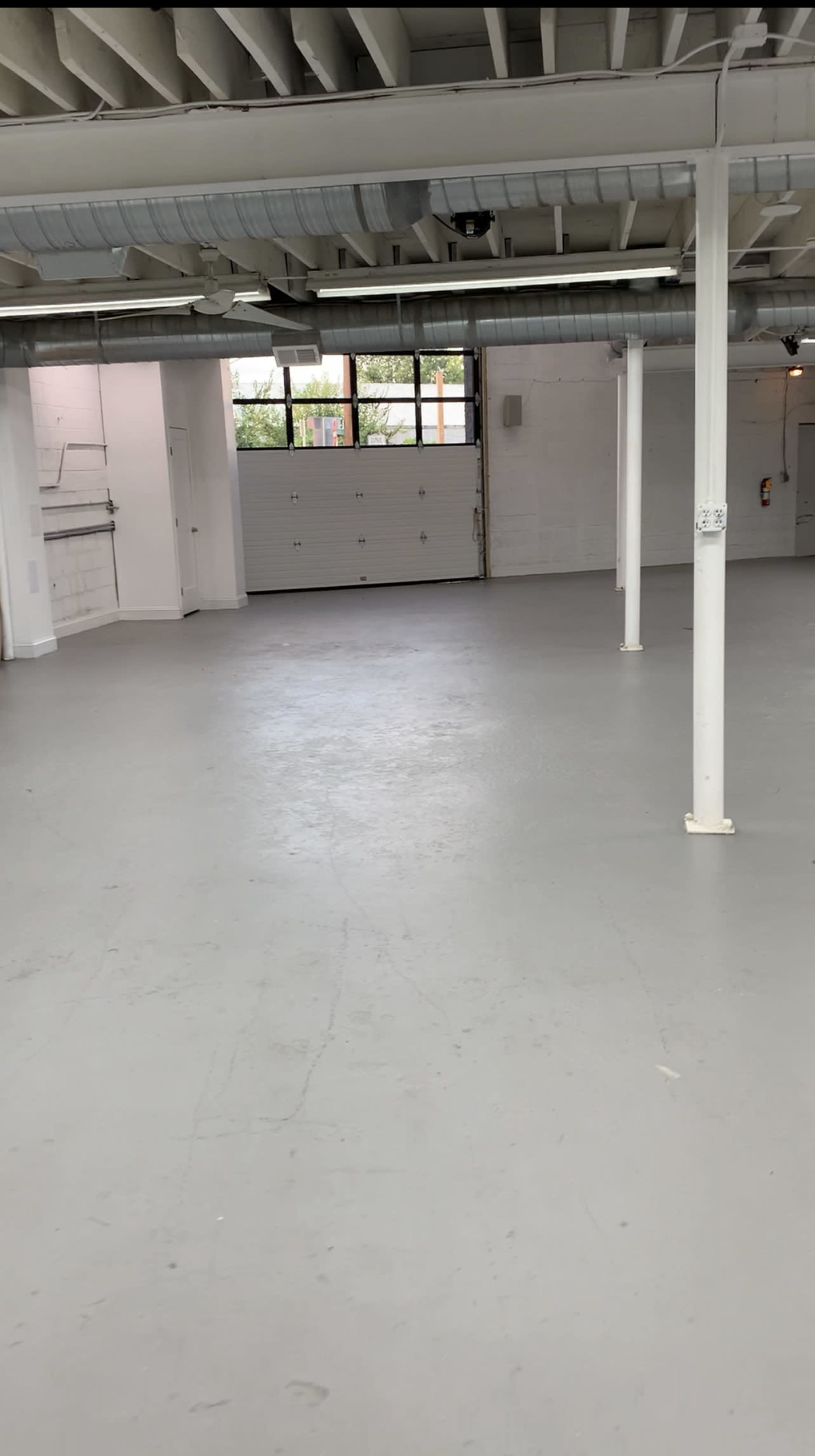 An empty, well-lit indoor space with a concrete floor, white walls, and large windows.