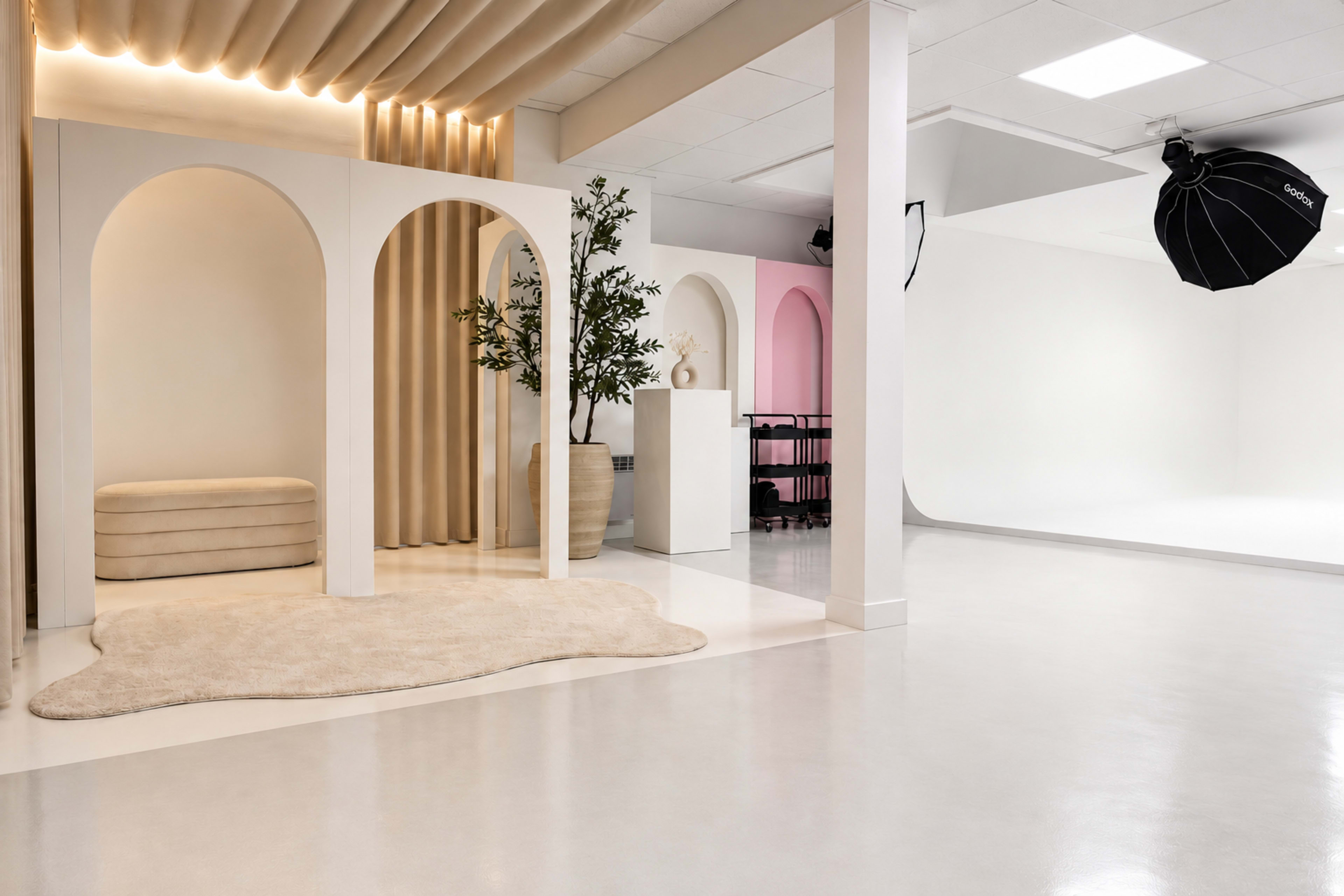 The image depicts a modern studio space featuring arched doorways, soft lighting, and minimalist furnishings, with a light-colored rug on the floor.