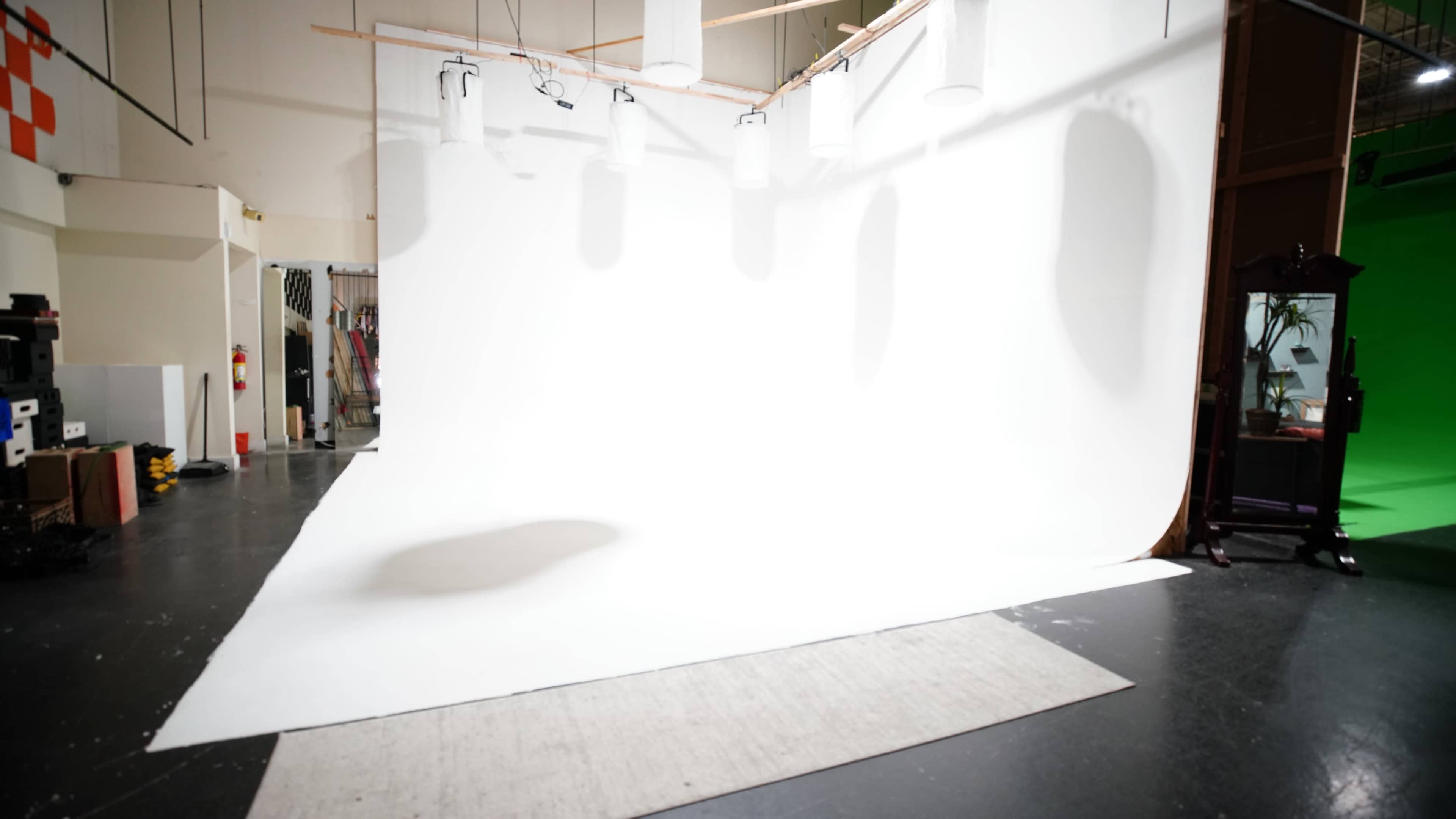 A photography studio with a white backdrop, spotlights, and a green screen on one side.