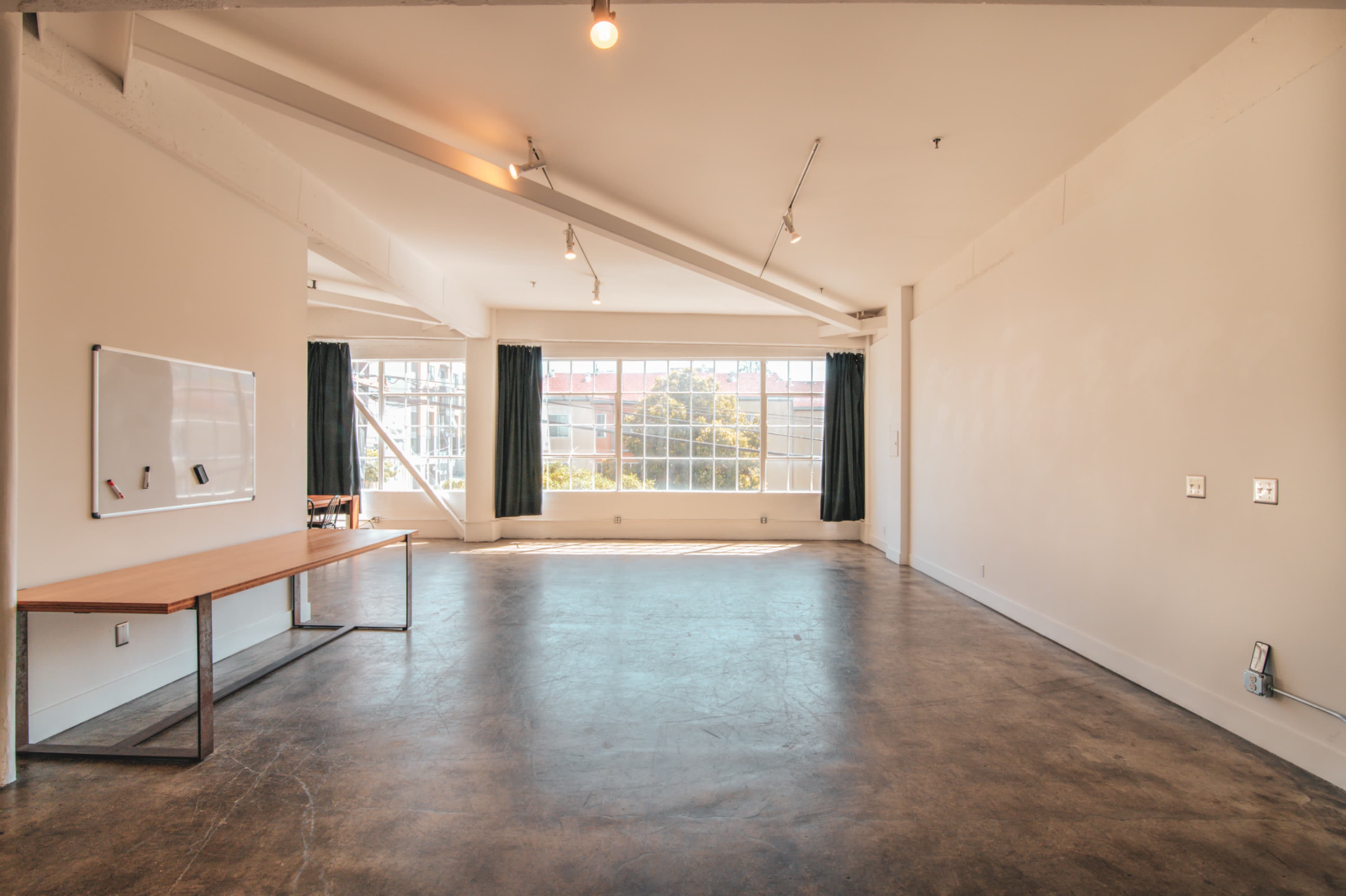 A spacious, modern room with large windows, a concrete floor, a wooden table, and minimalistic decor.