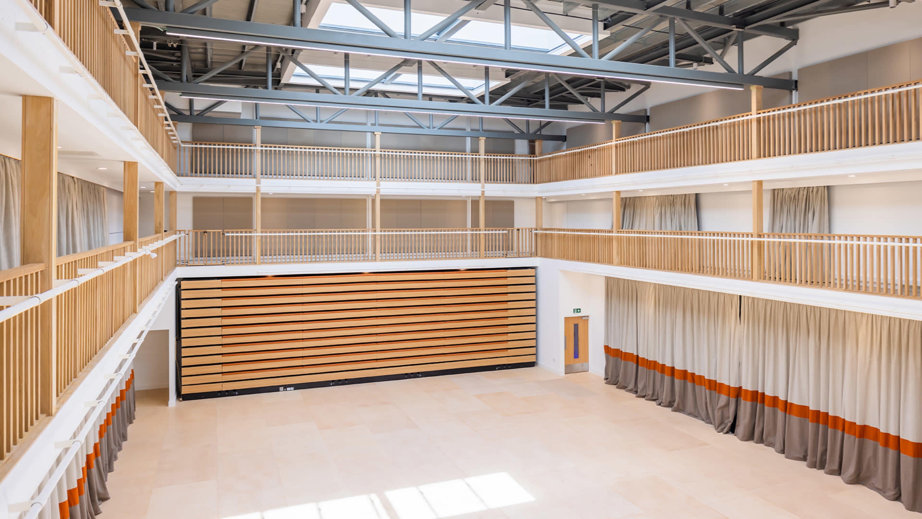 A spacious interior with multiple levels and wooden railings, featuring a high ceiling with skylights and a large wall of curtain-covered panels.