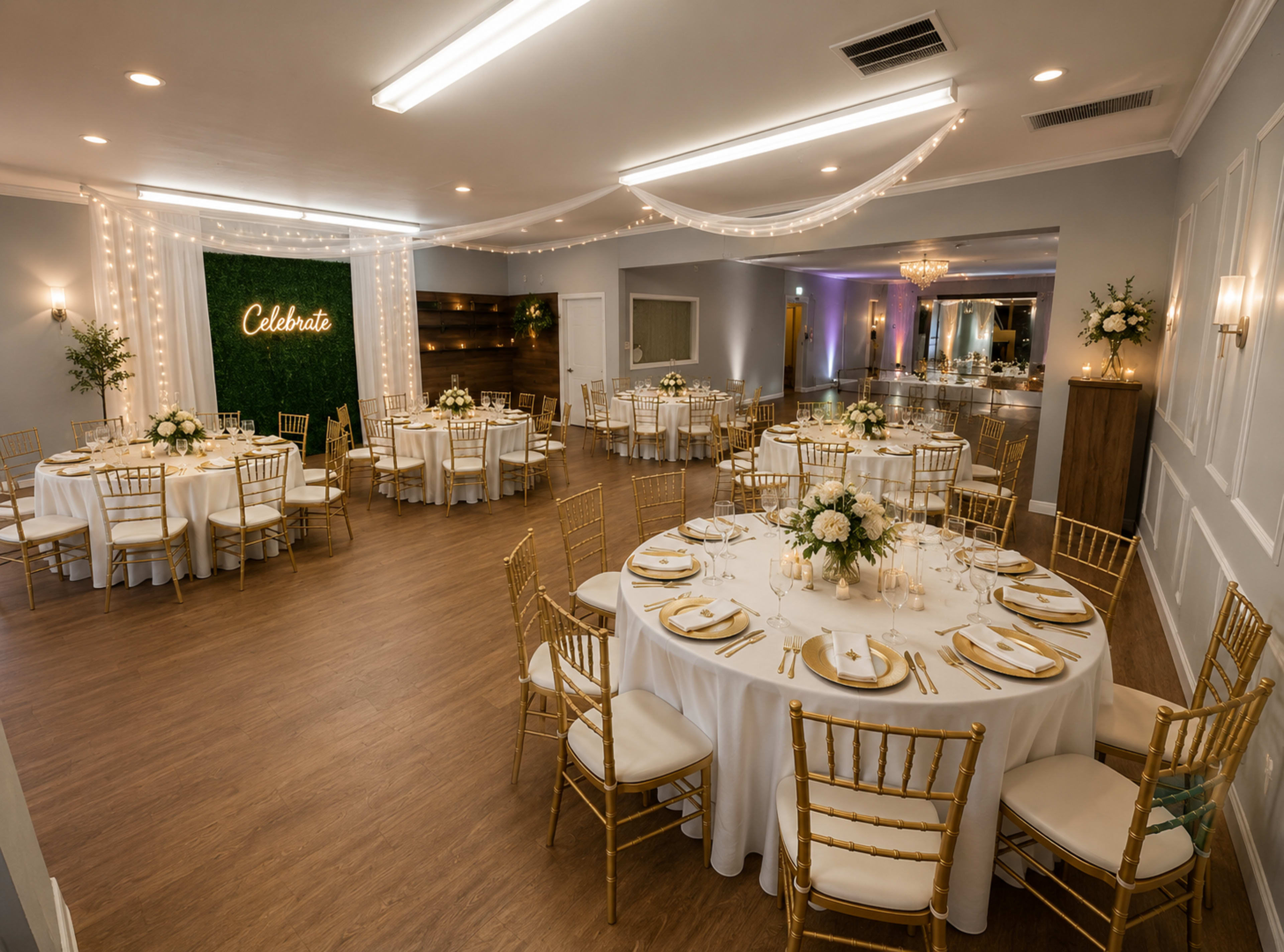 The image shows a elegantly decorated event space with round tables covered in white tablecloths, gold chairs, and a backdrop that reads "Celebrate" surrounded by greenery.