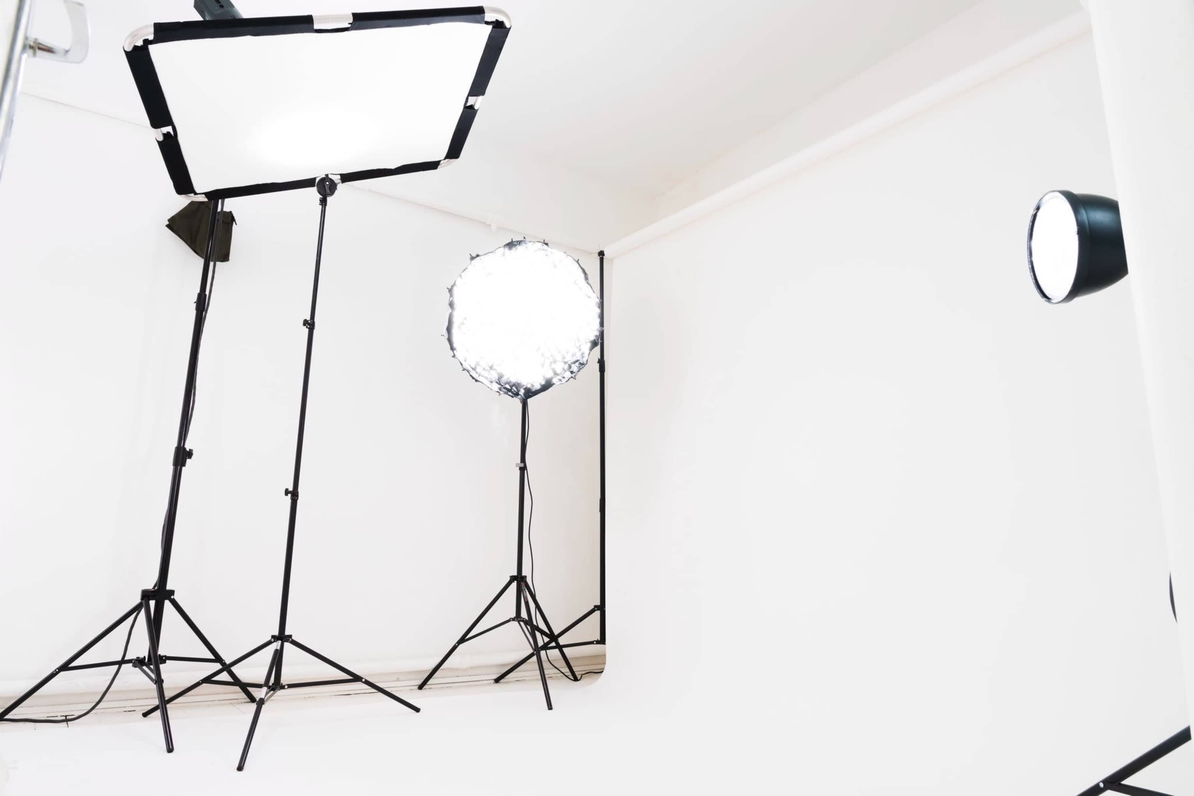The image shows a photography studio with three lighting setups positioned on a plain white backdrop.