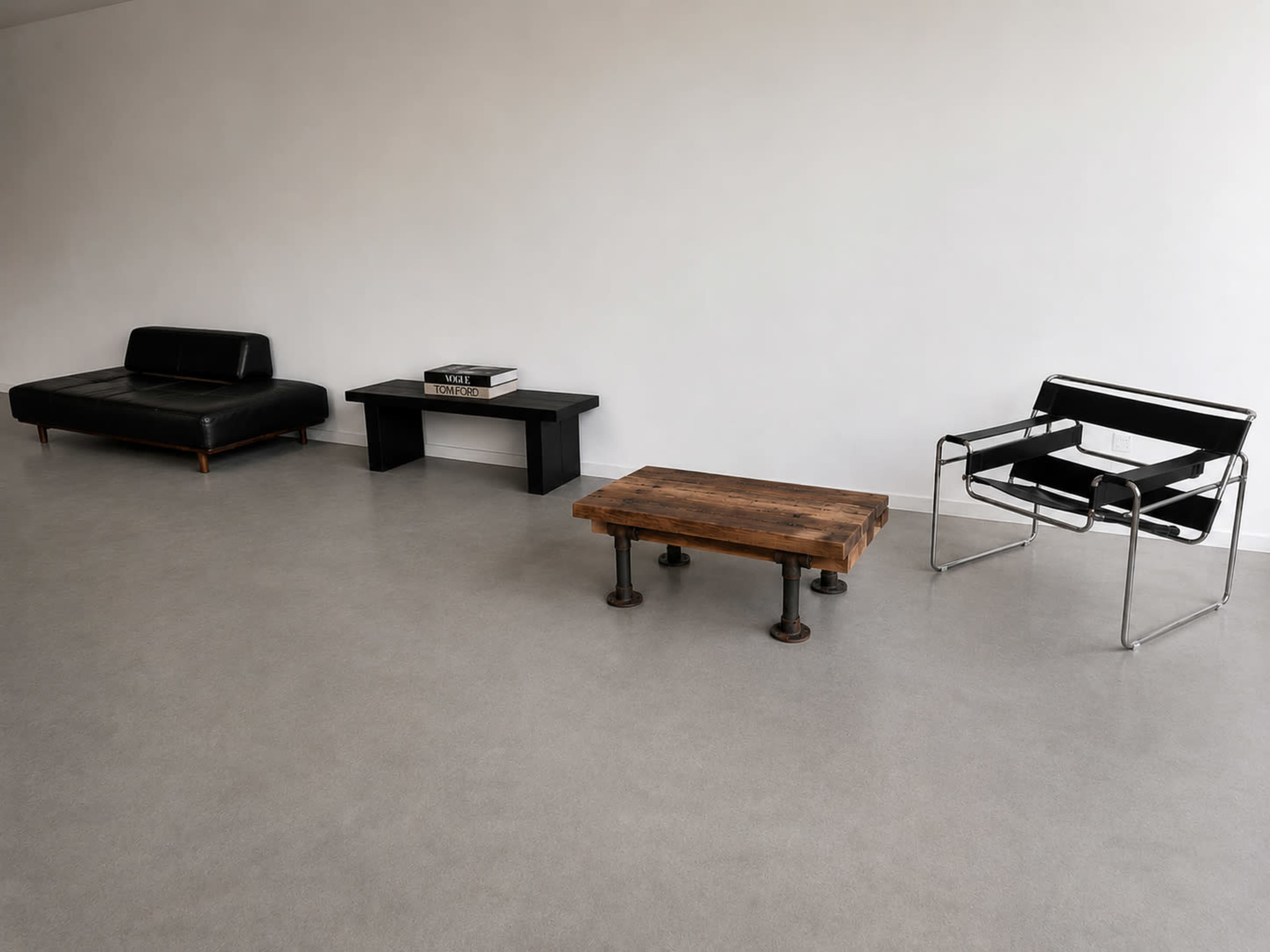 The image shows a minimalist interior featuring a black leather sofa, a wooden coffee table supported by metal pipes, a black console table, and a modern metal chair, set against a plain white wall.