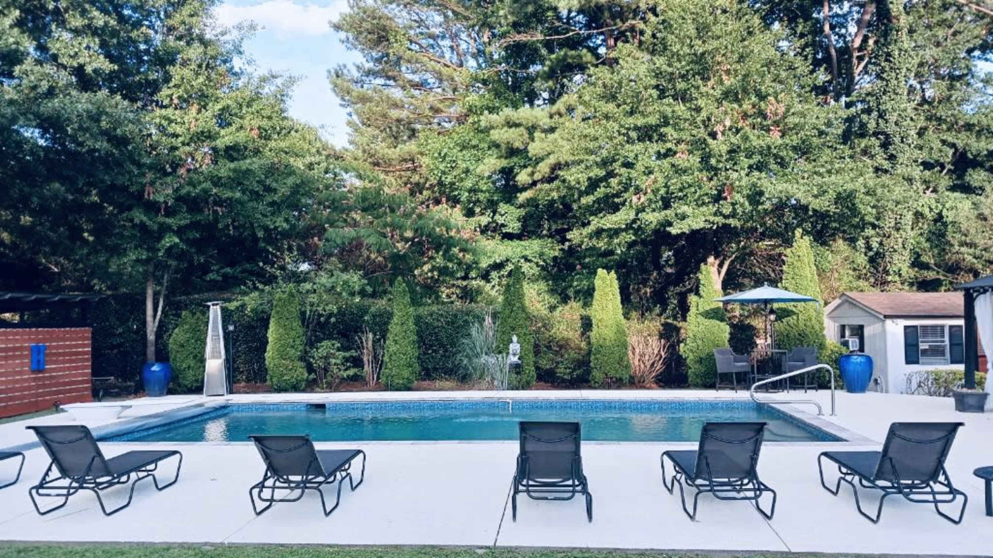 A swimming pool area surrounded by green trees, lounge chairs, and decorative plants.