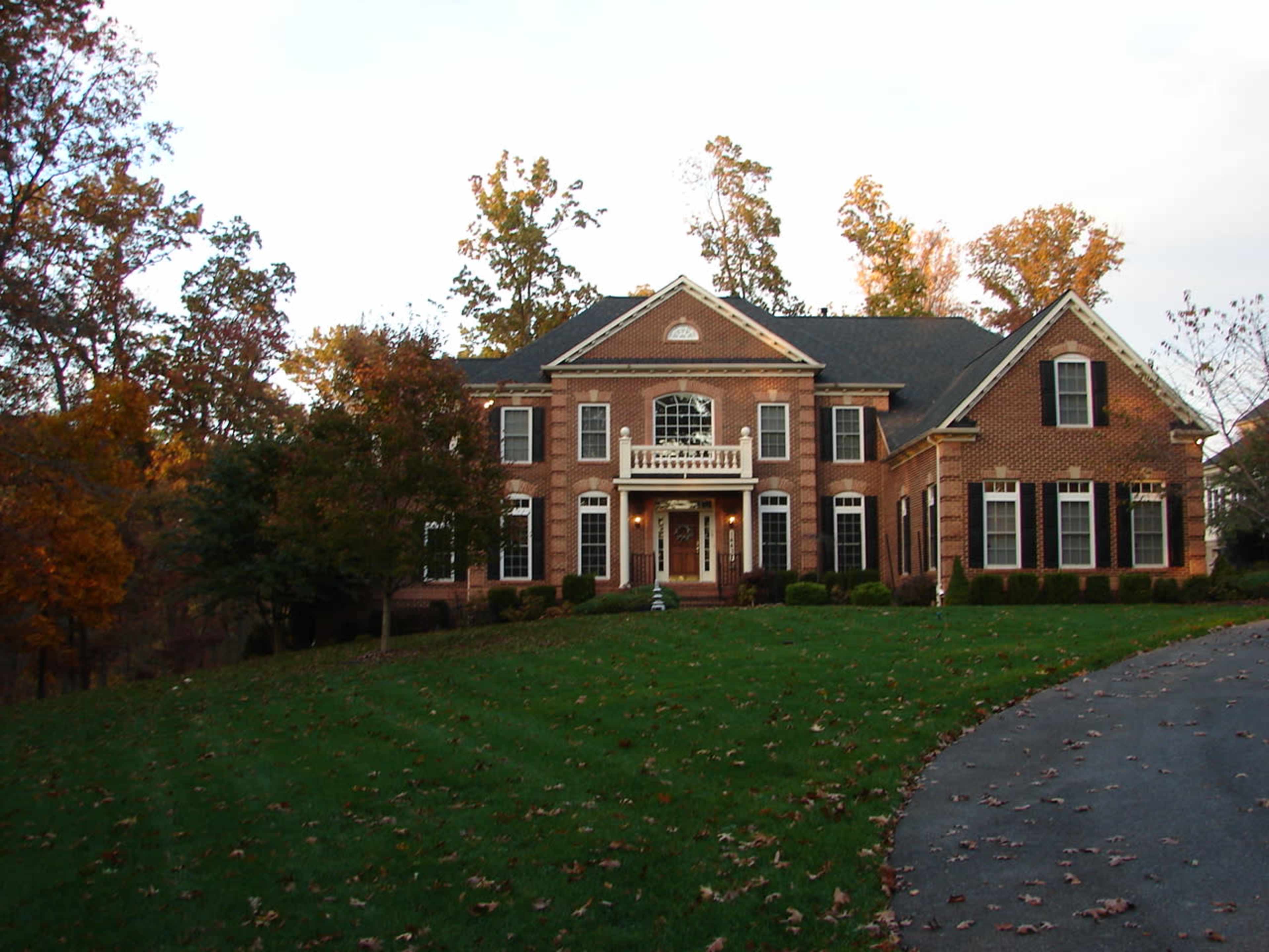 A large brick house with a well-manicured lawn and trees in autumn foliage surrounding it.