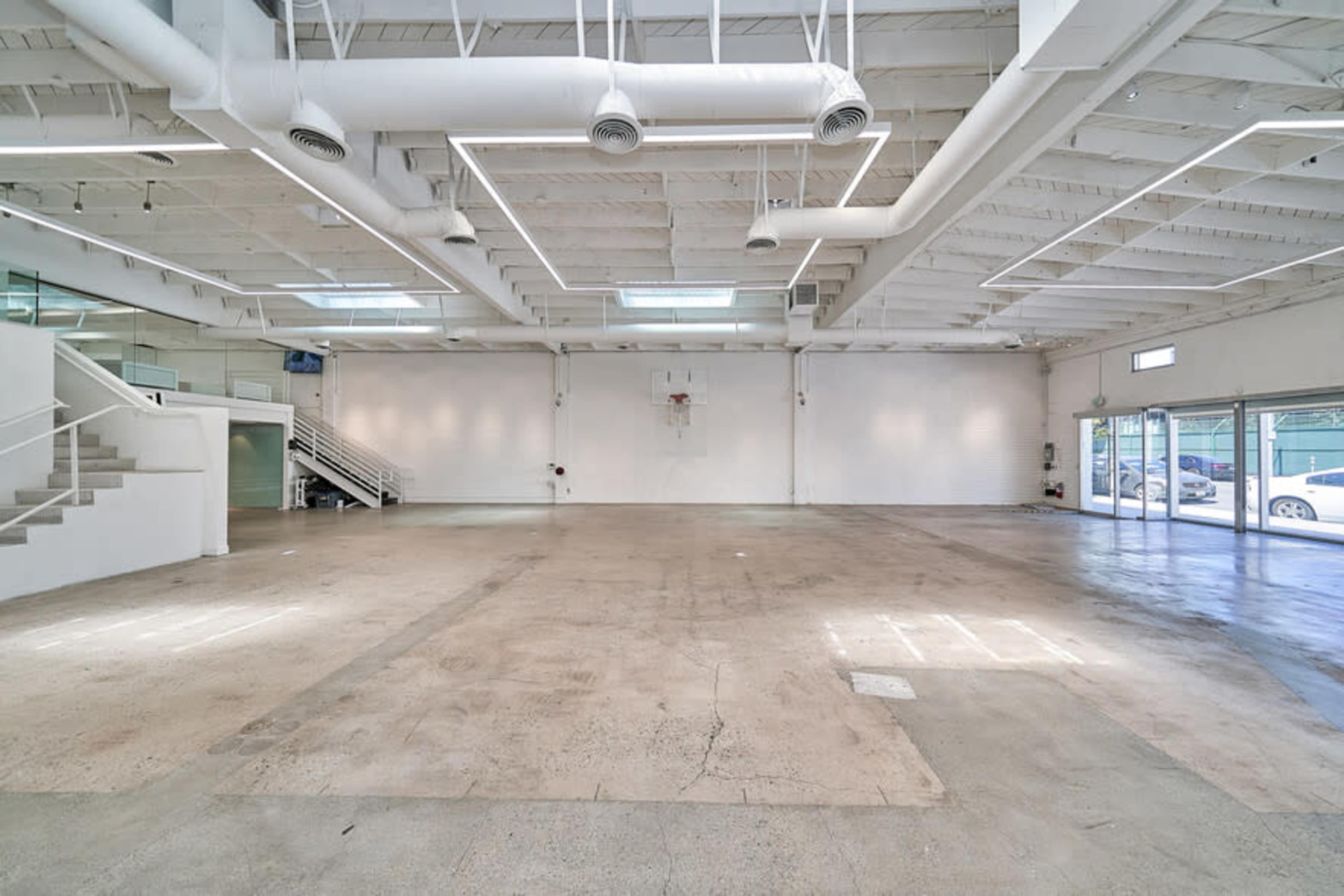 A spacious, empty interior of a commercial building with high ceilings, large windows, and a smooth concrete floor.
