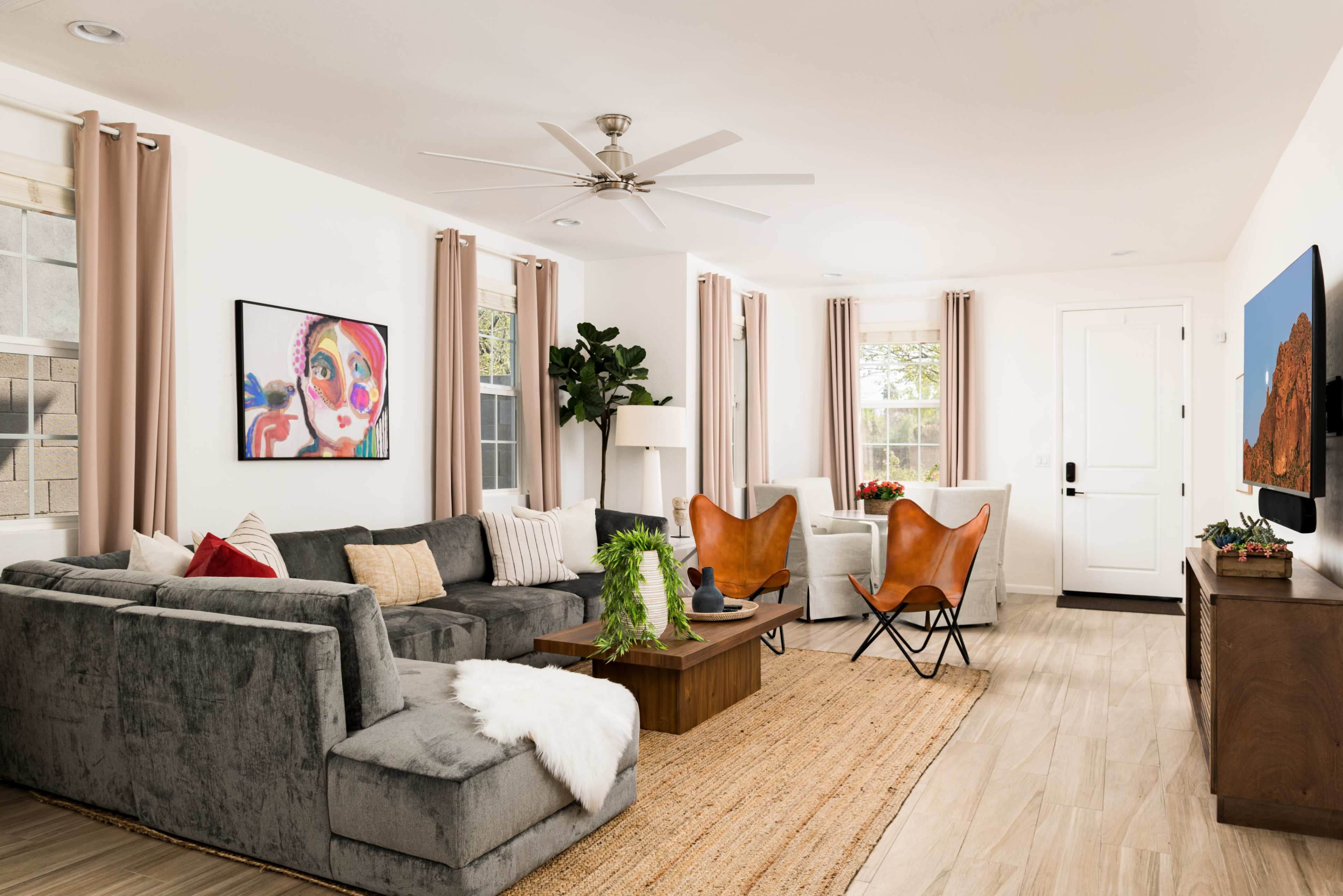 The living room features a gray sectional sofa, two butterfly chairs, a wooden coffee table, and large windows with light curtains.