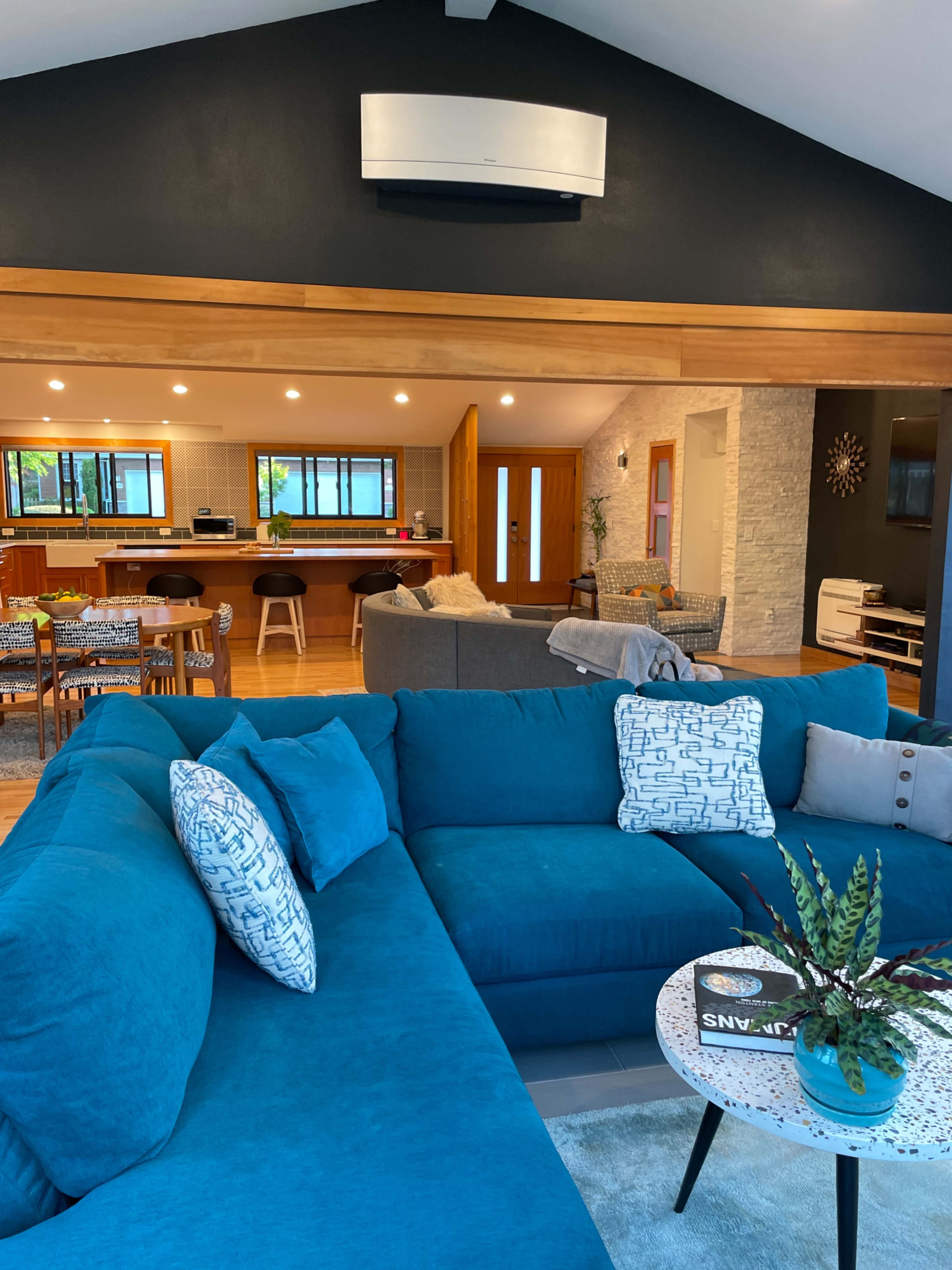 A spacious living room with a turquoise sectional sofa, a round coffee table, and an open kitchen area visible in the background.