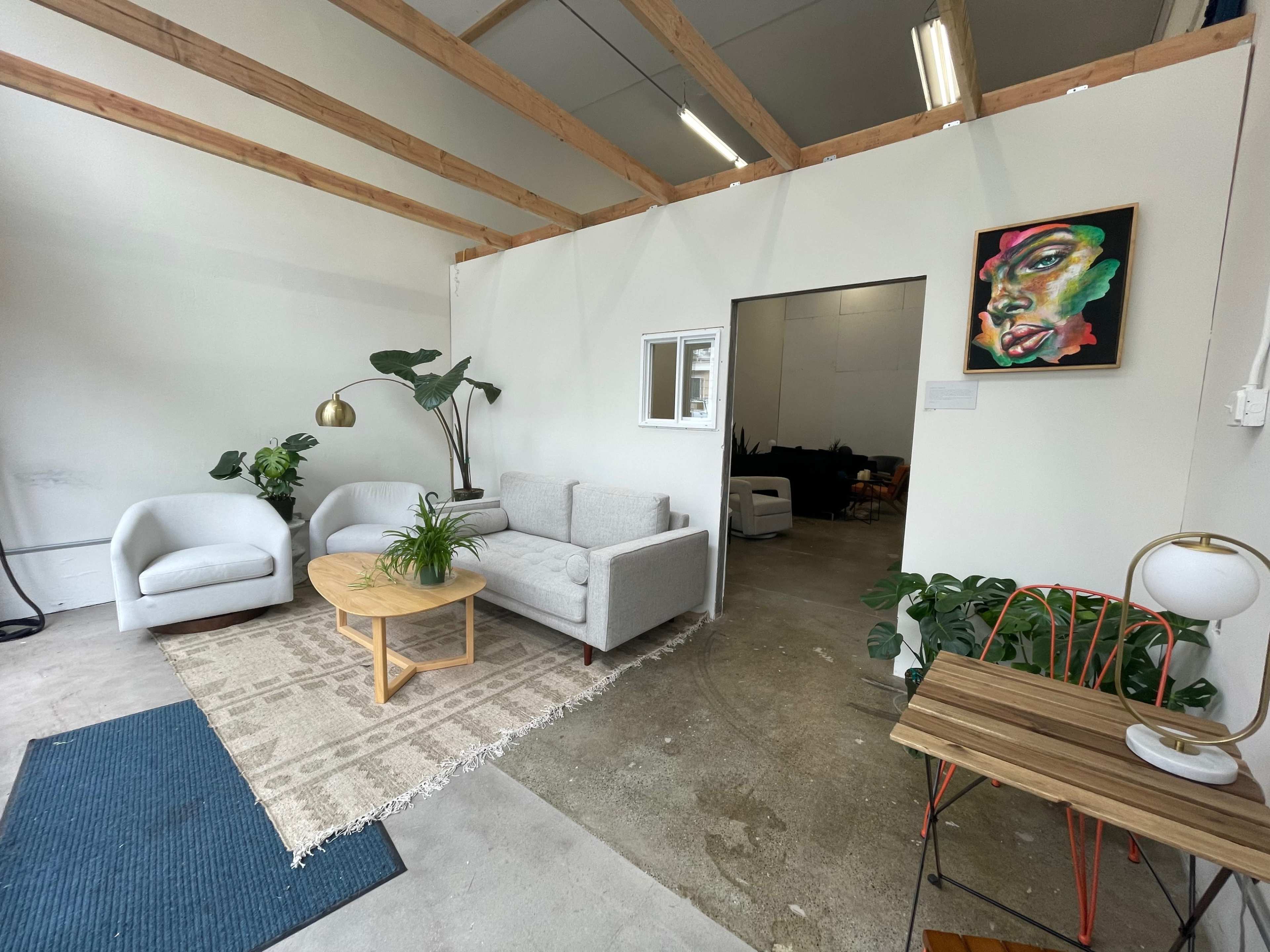 A modern, minimalistic interior space with a seating area that includes a light gray sofa, two white armchairs, a round wooden table, and decorative plants.