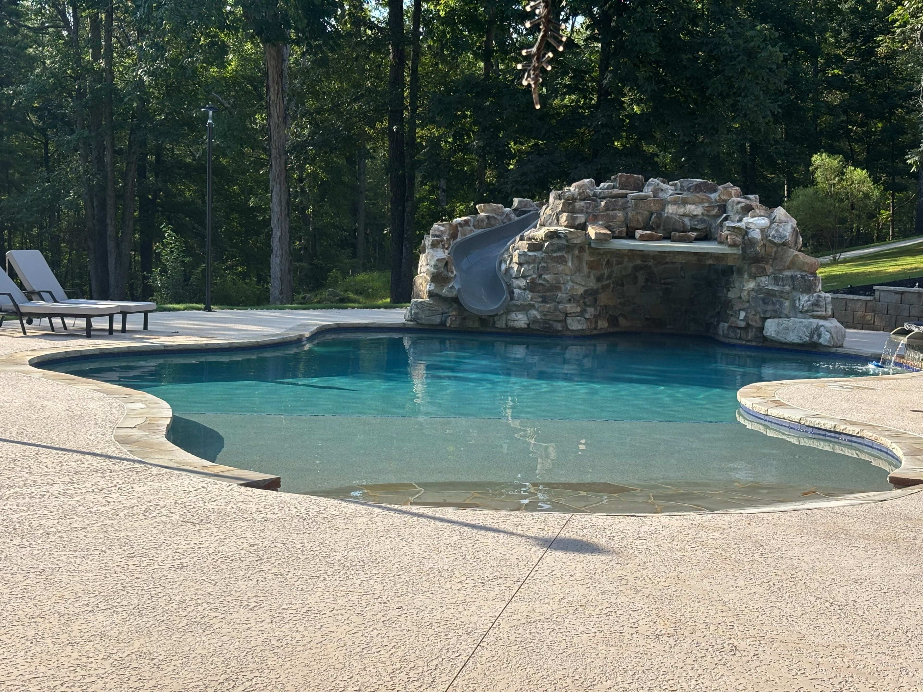 The image shows a swimming pool with a rock slide and a landscaped area surrounded by trees.