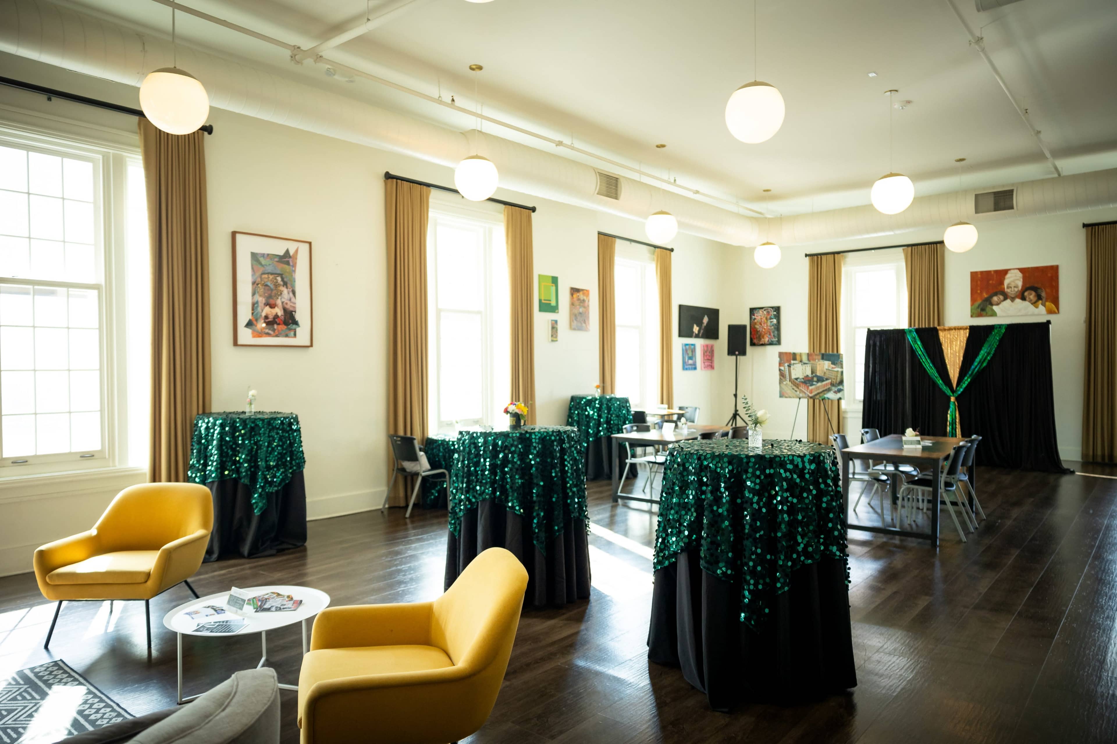 The room features a spacious layout with decorated tables, vibrant artworks on the walls, and a black backdrop adorned with green and gold embellishments.