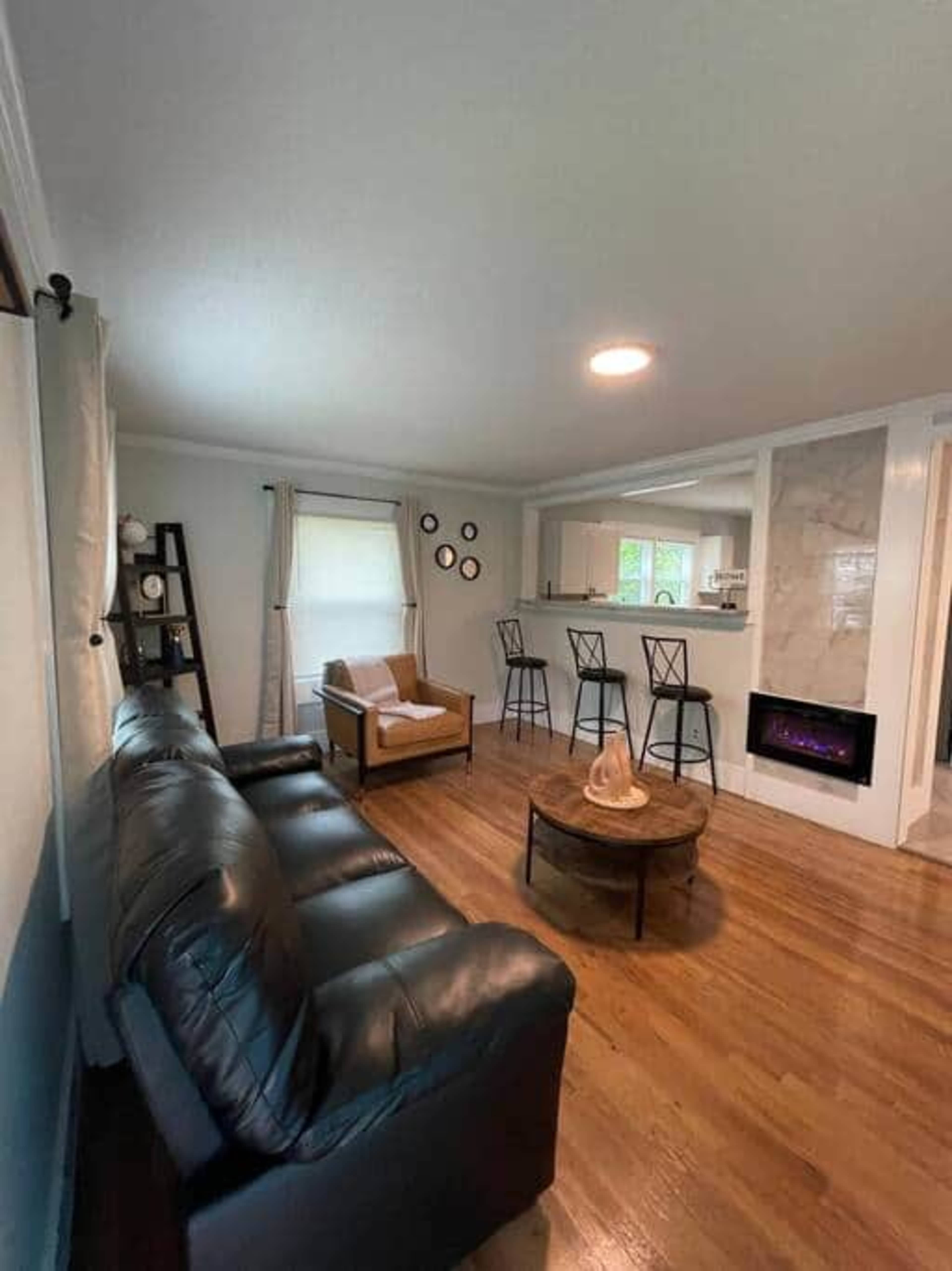 A living room with a black leather couch, a brown armchair, a round coffee table, and a short bar counter with three stools.