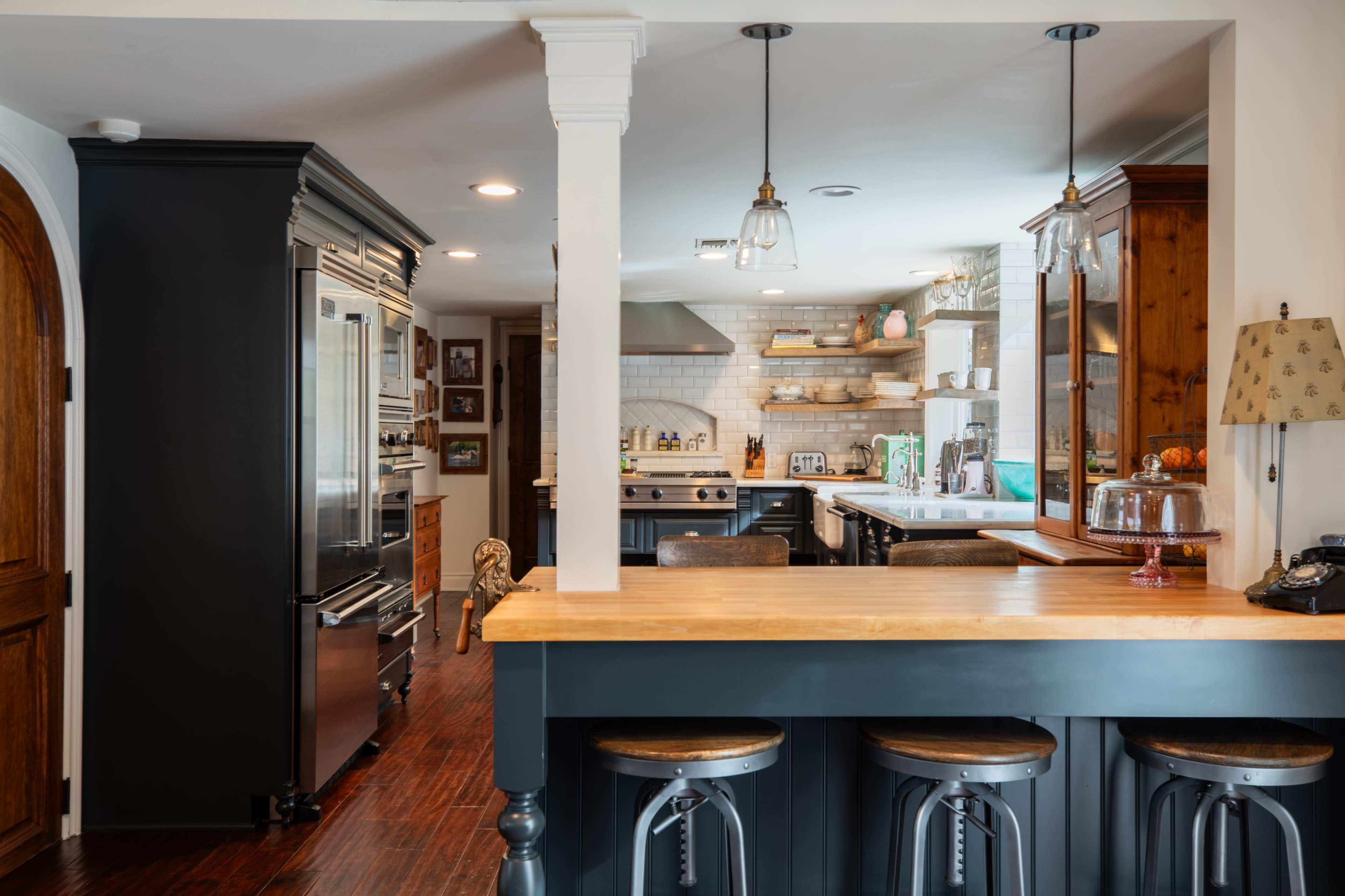 The image shows a modern kitchen featuring dark cabinetry, a wooden island with bar stools, and stainless steel appliances.