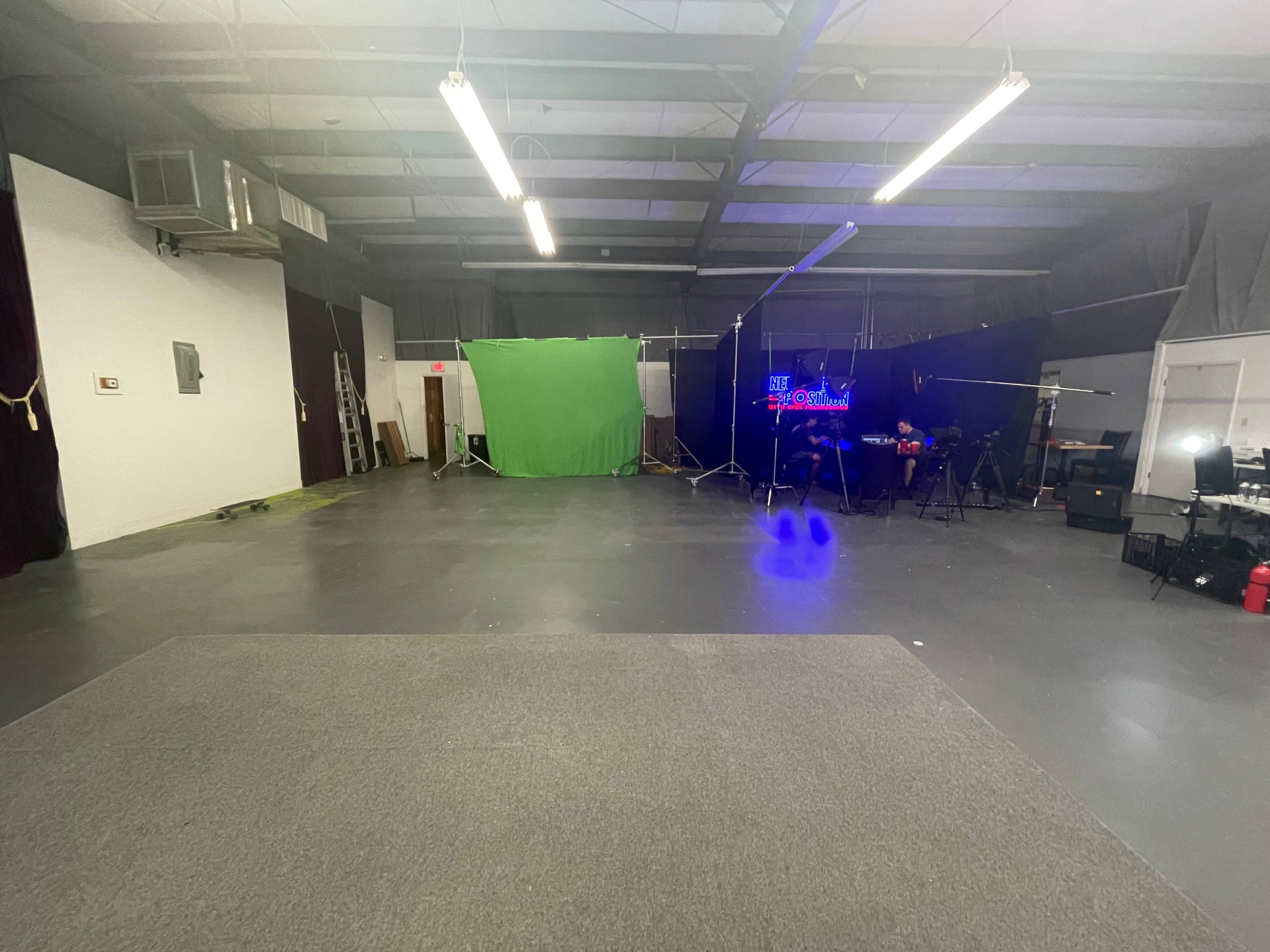 An empty studio space with a green screen setup, lighting equipment, and various cameras arranged along the walls.