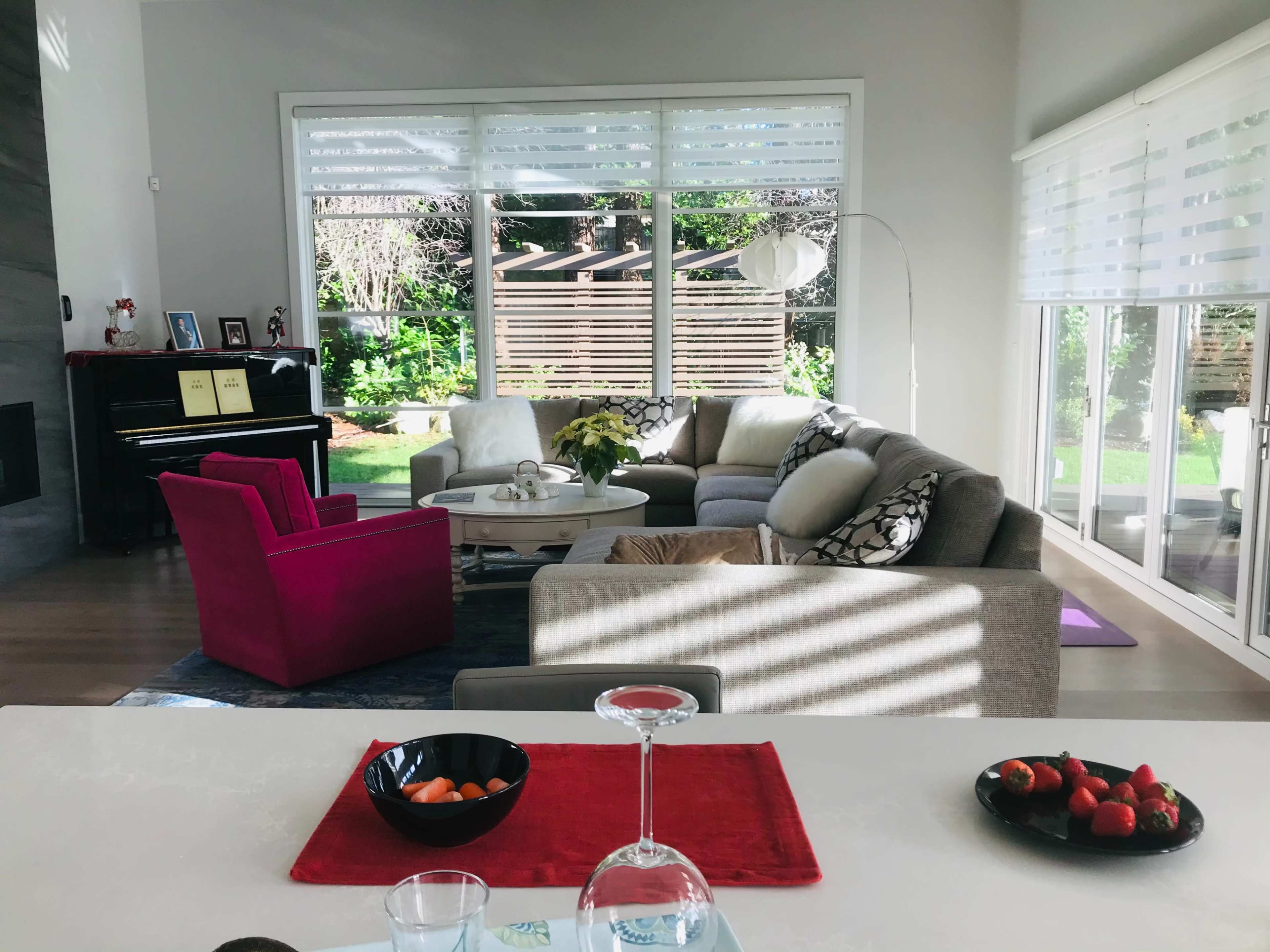 A modern living room with a mix of gray and pink furniture, large windows, and a view of a garden outside.