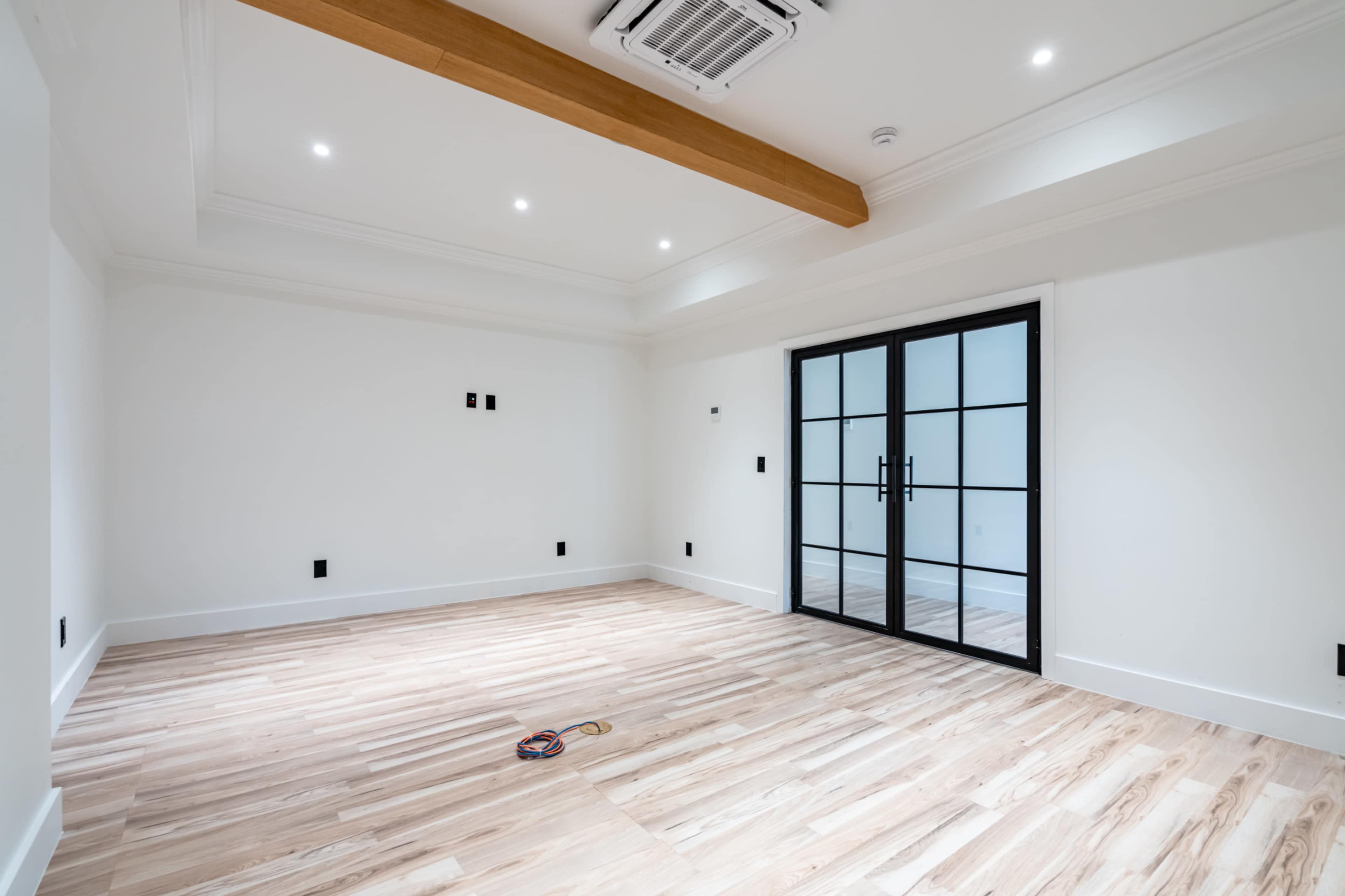 A spacious, empty room with wooden flooring and a large glass door leading to another area.