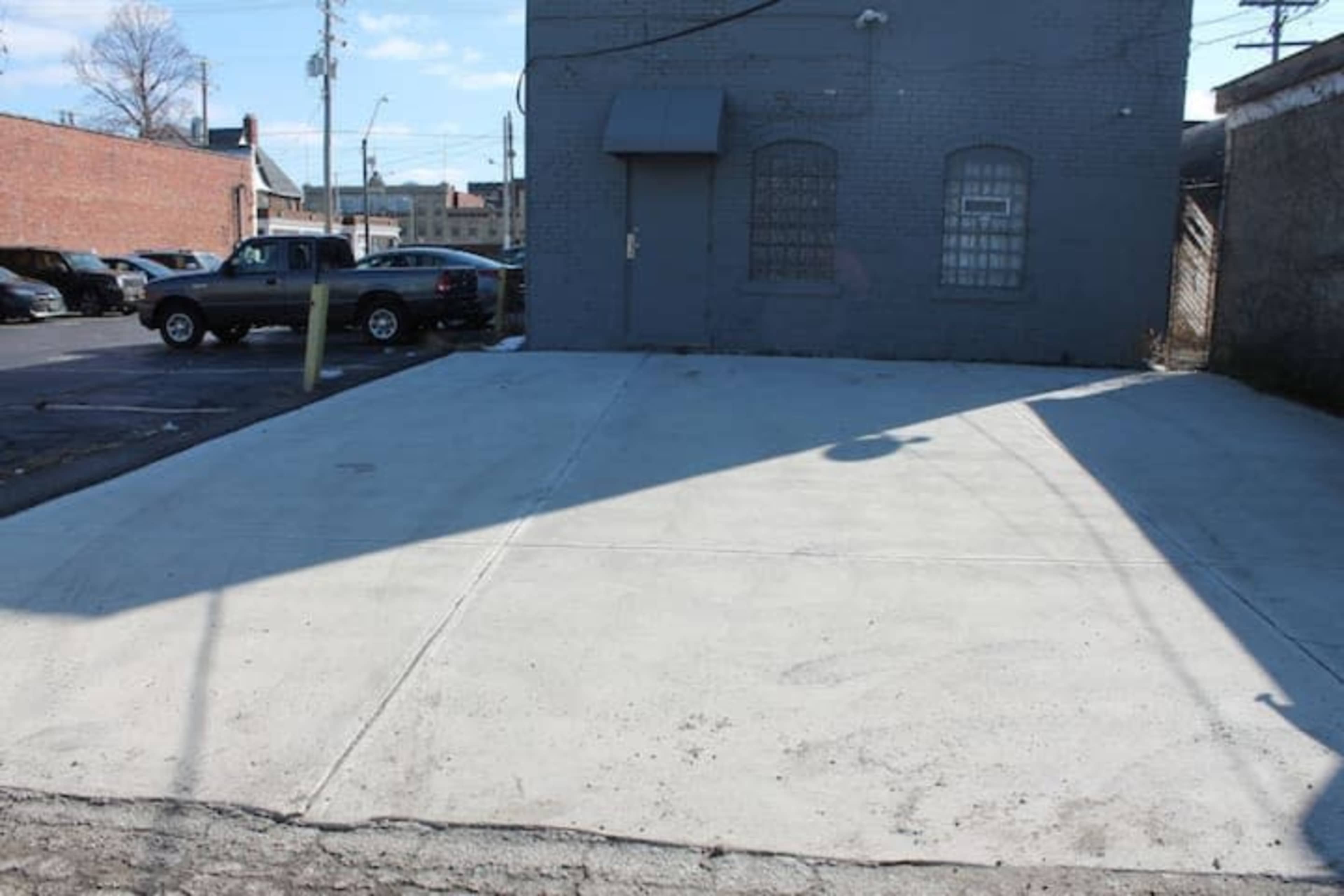 A concrete parking lot is situated beside a gray building with a door and two small windows.