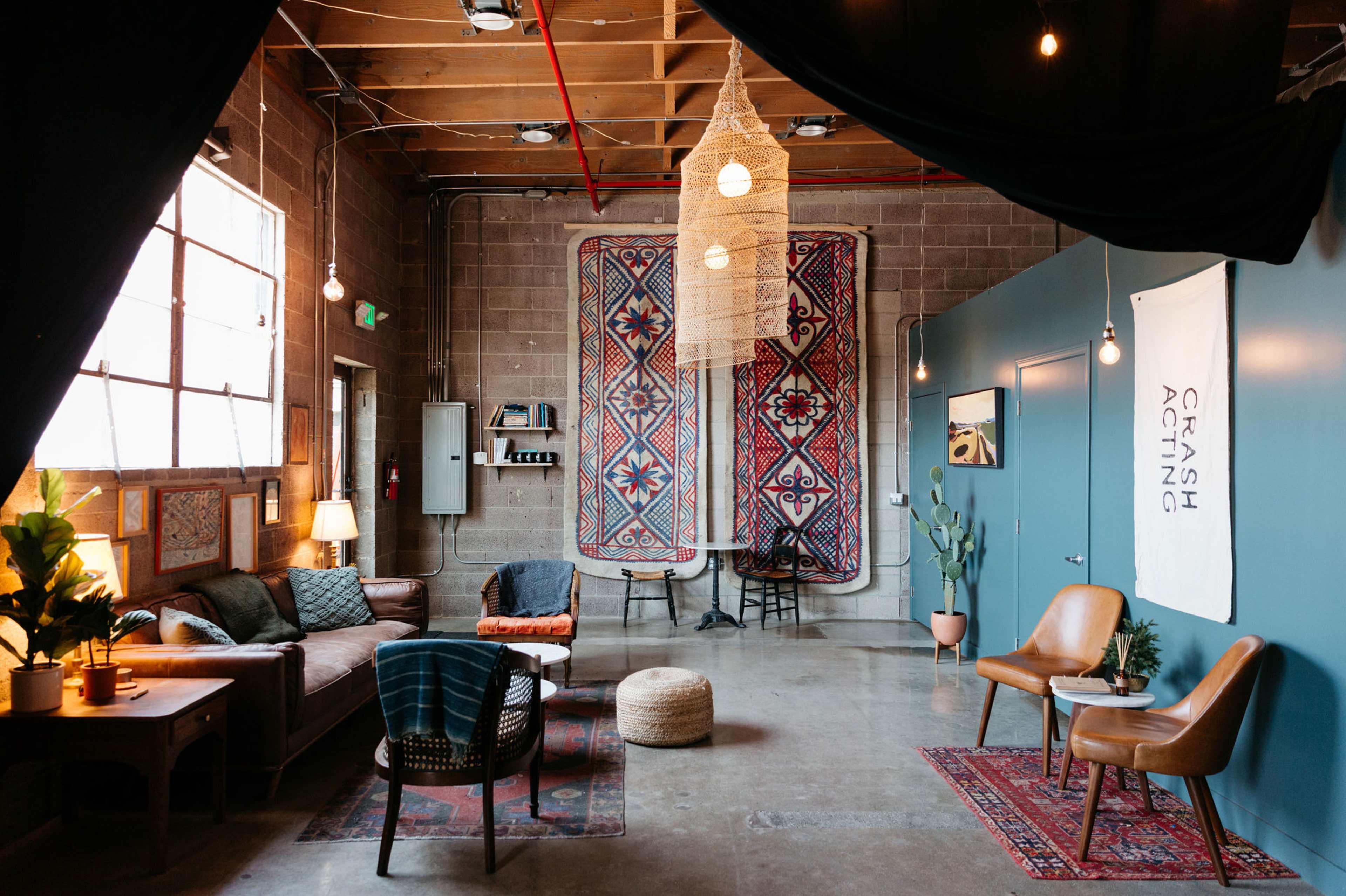 A cozy sitting area with a patterned rug, various seating options, and decorative wall hangings in an industrial-style room.
