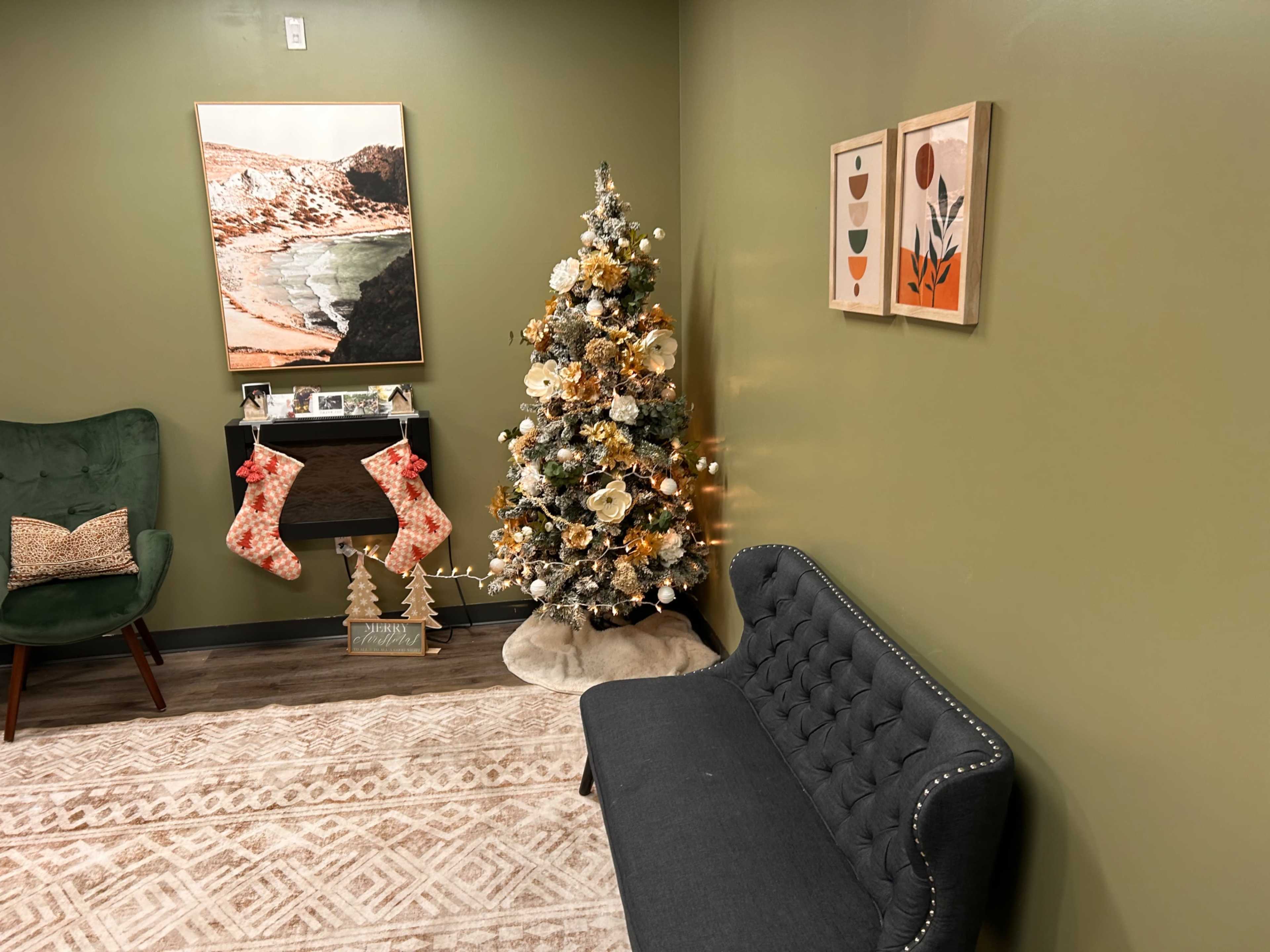The image shows a cozy room with a decorated Christmas tree, two stockings hanging, and a green accent wall, featuring a sofa and artwork.