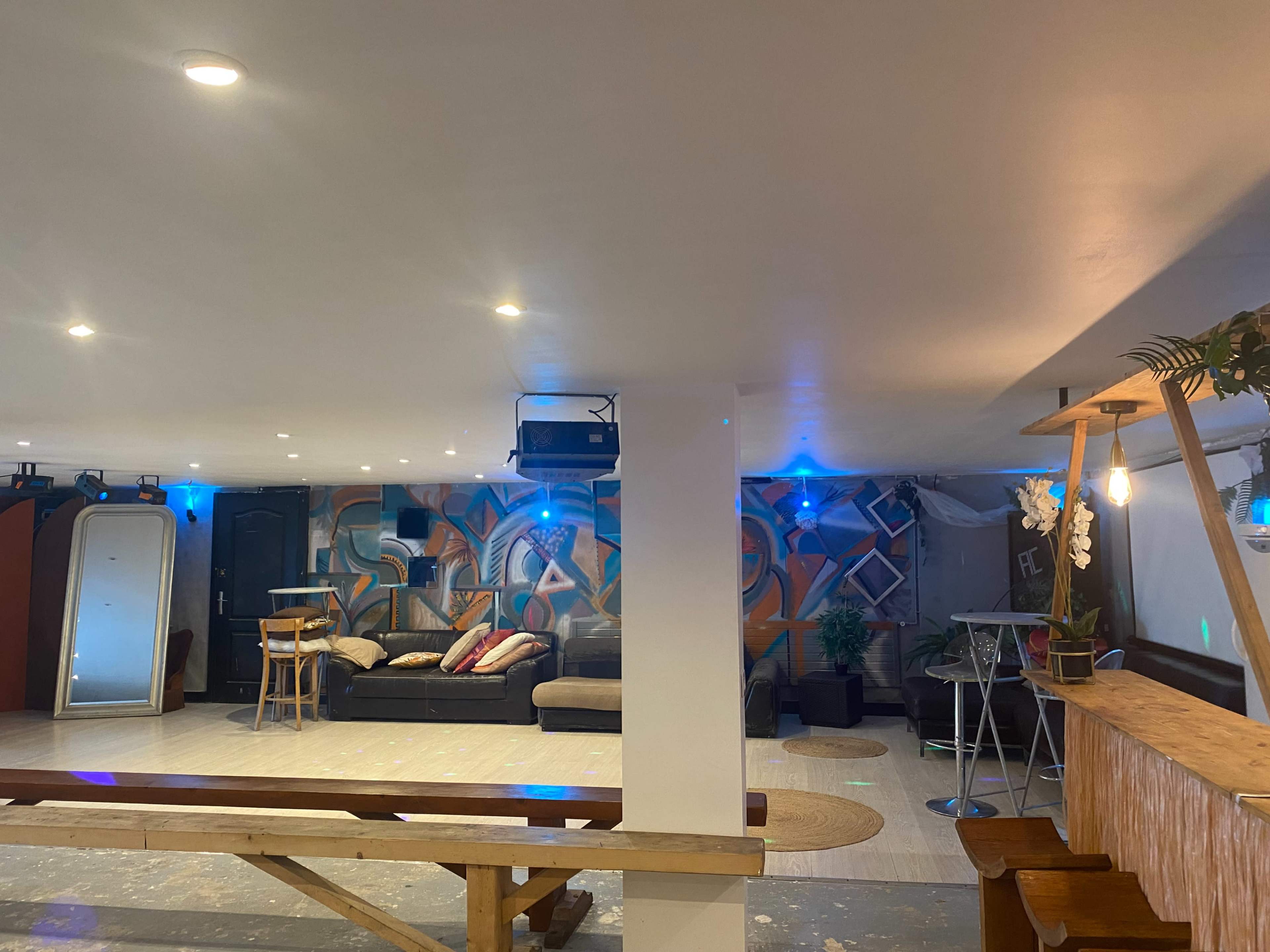An indoor space featuring a mural on the wall, seating areas with cushions, and illuminated tables arranged for social gatherings.