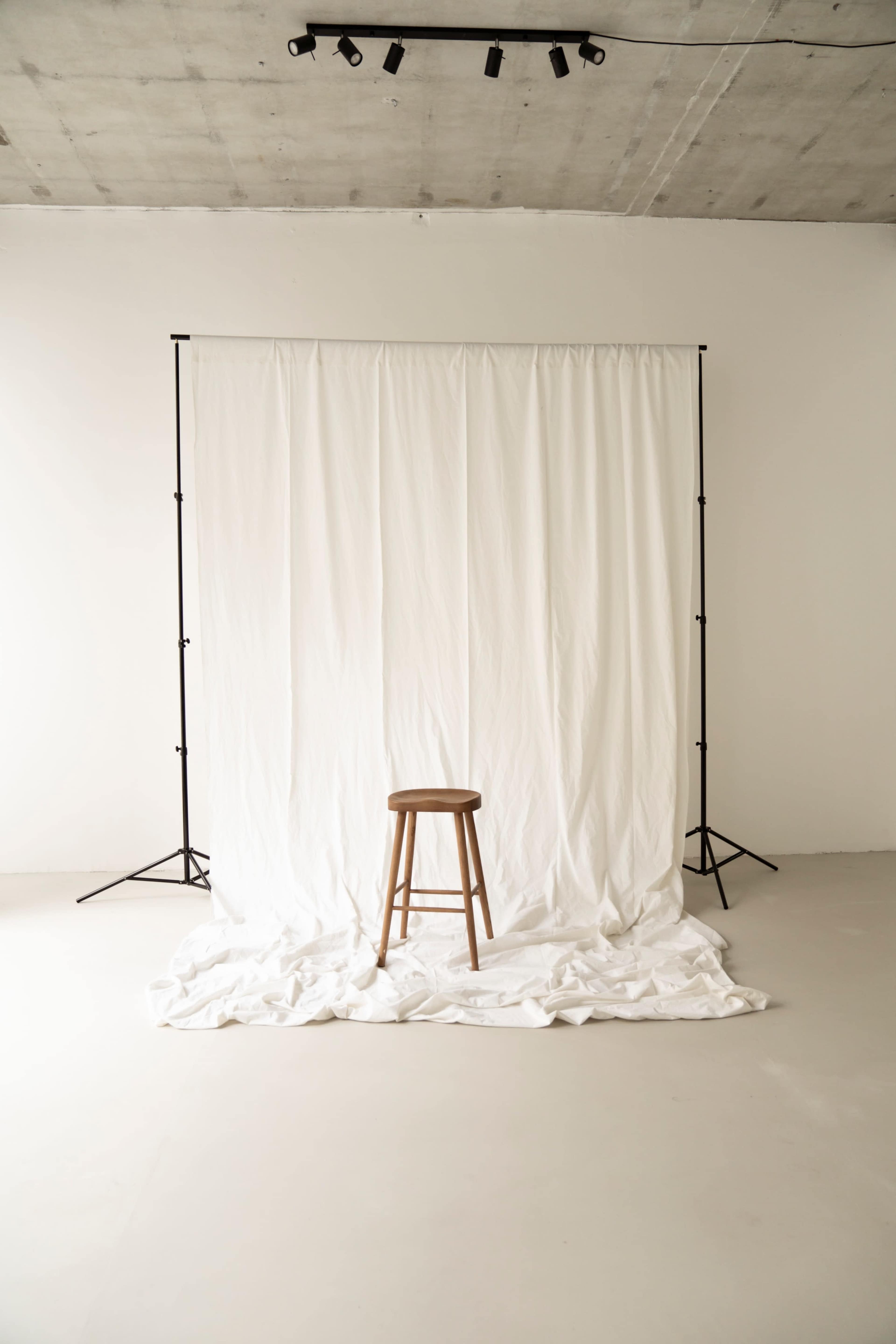 A wooden stool is positioned in front of a white backdrop draped on the floor.
