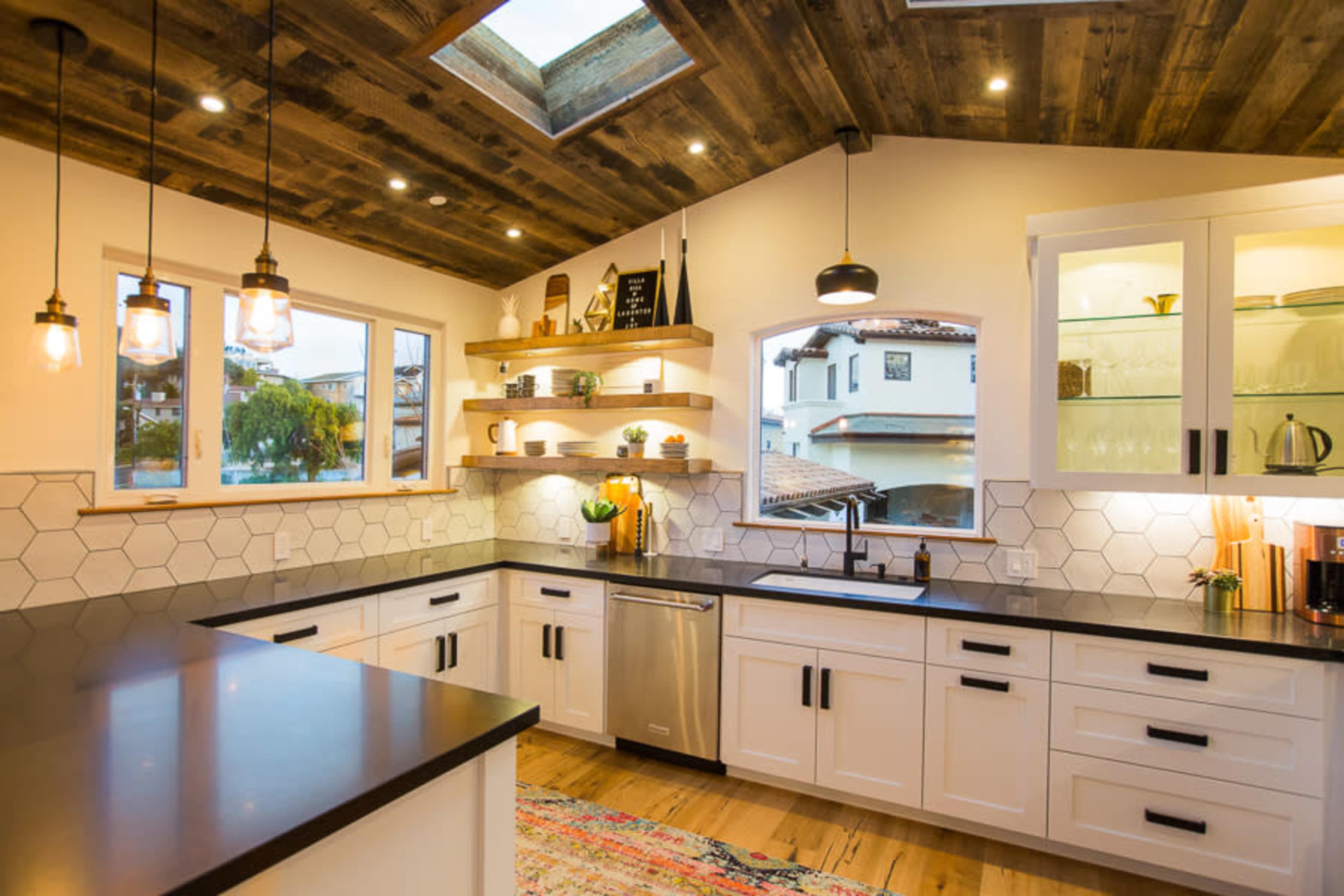 The kitchen features a modern design with white cabinets, a dark countertop, and hexagonal backsplash tiles, illuminated by pendant lighting and a skylight.