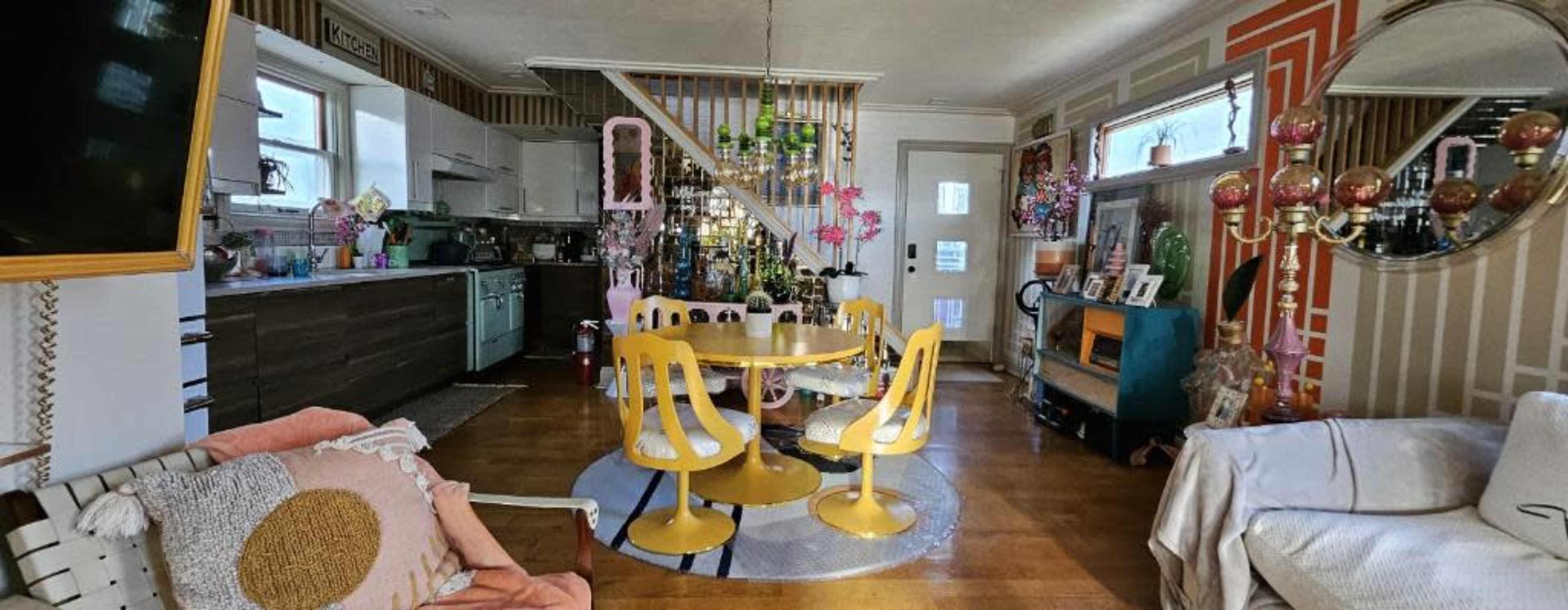 A colorful living space featuring a yellow circular dining table with matching chairs, a white sofa, and various decorative items throughout the room.