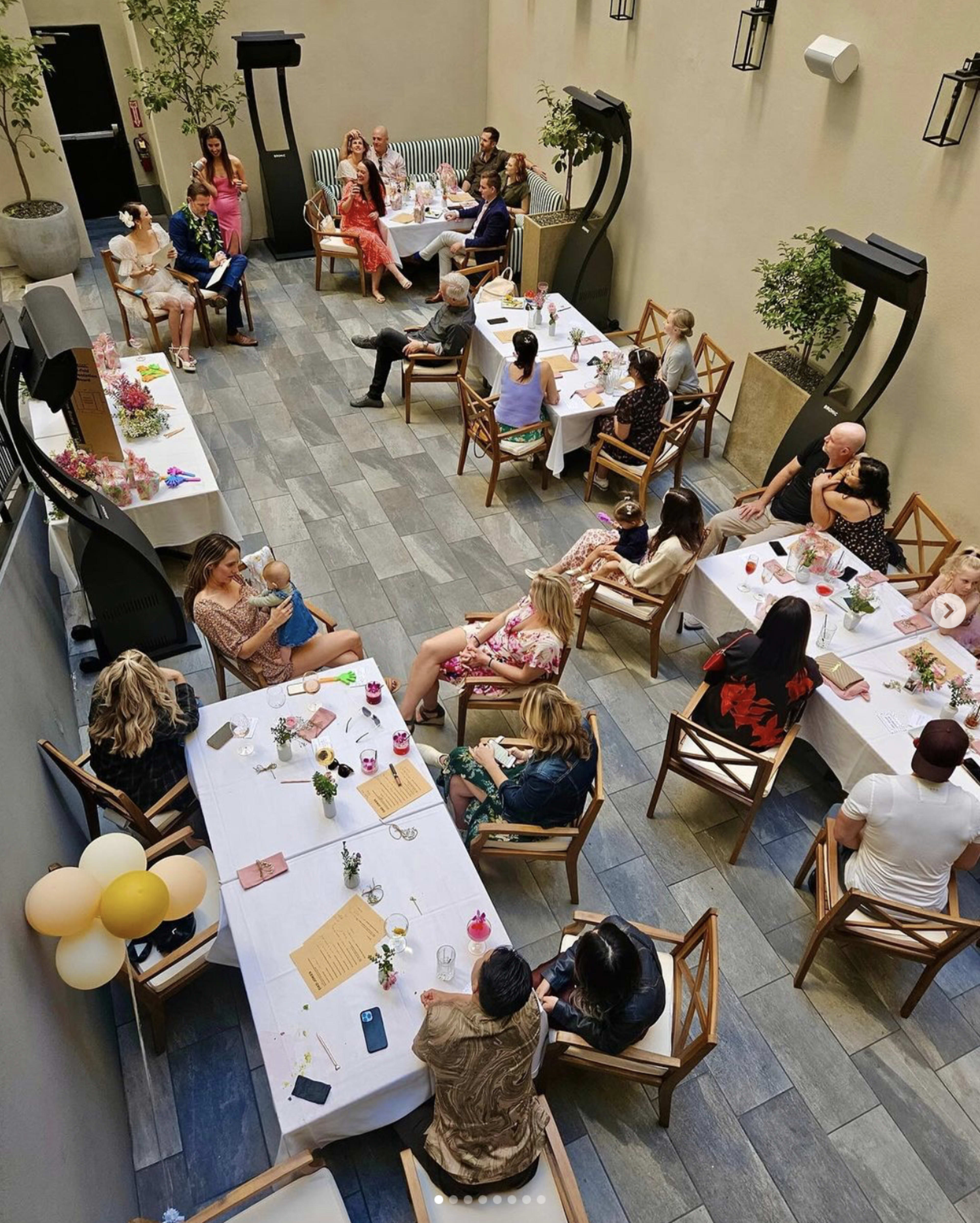 A gathering of people seated at tables in a narrow, well-lit courtyard.