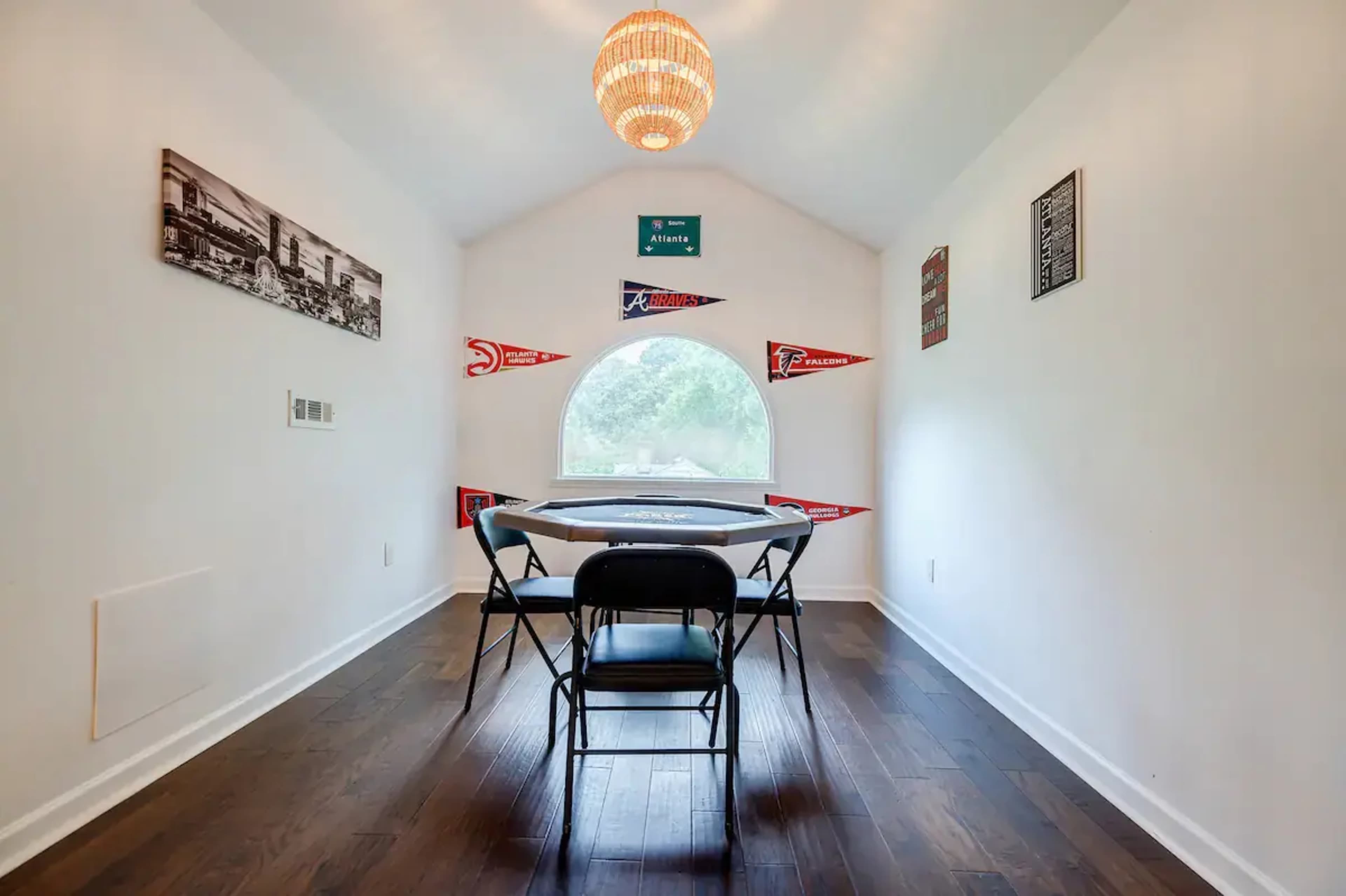 A small room with a round window, a table covered with a tablecloth, and black folding chairs arranged around it, decorated with sports pennants on the walls.