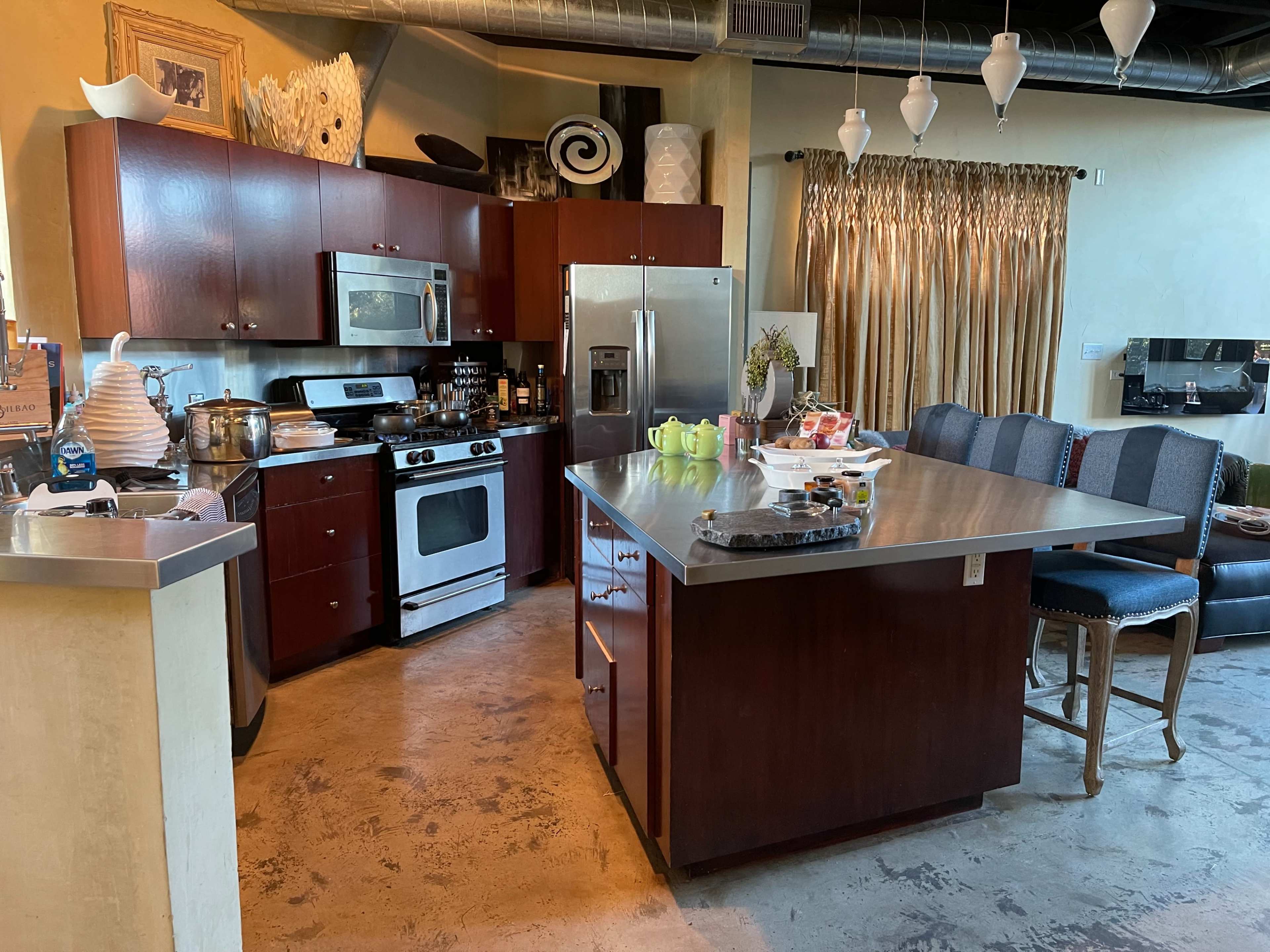The image shows a modern kitchen with dark wood cabinetry, stainless steel appliances, and a large central island with a silver countertop.