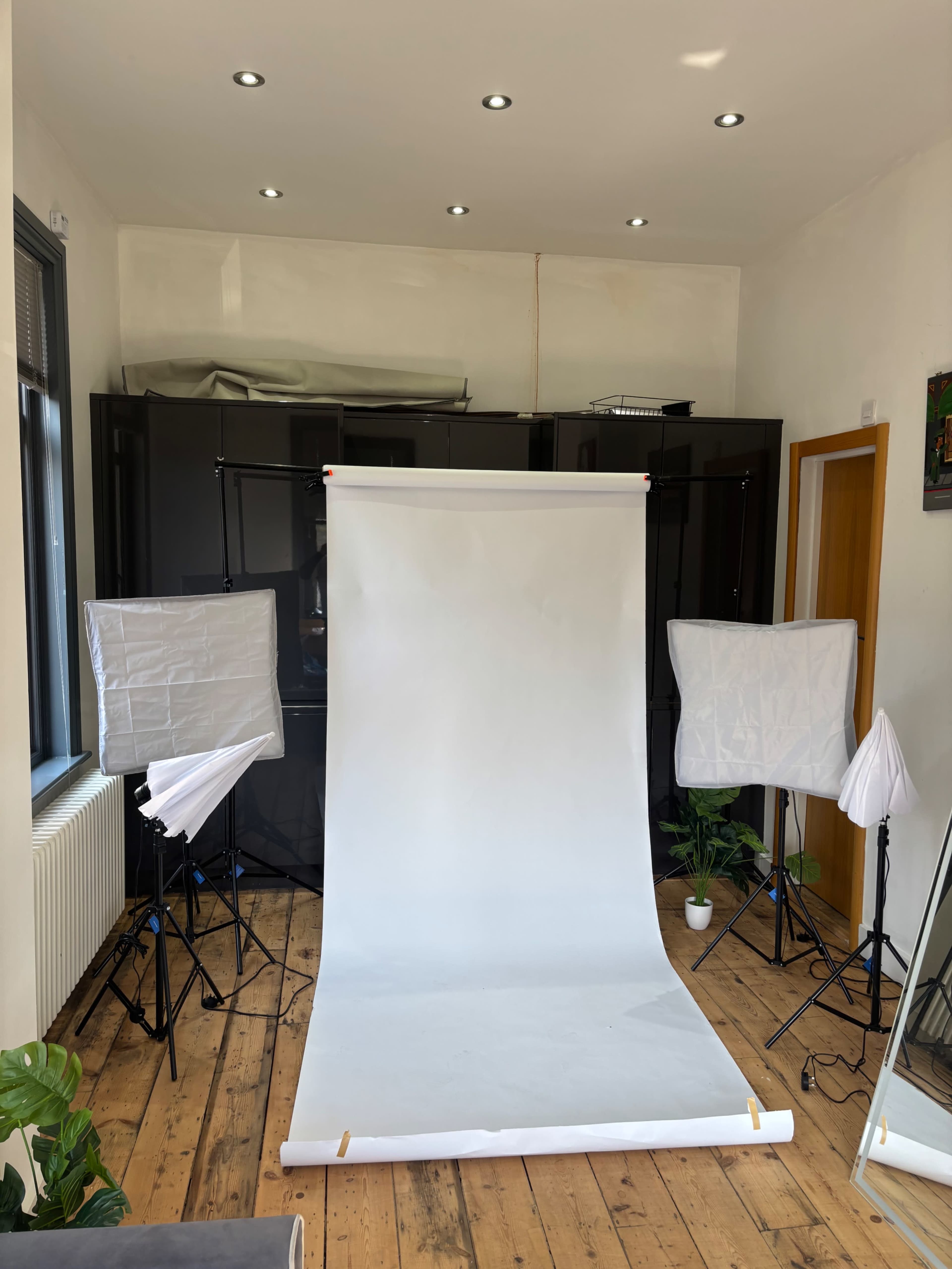 A photography studio is set up with a white backdrop, softbox lights, and wooden flooring.