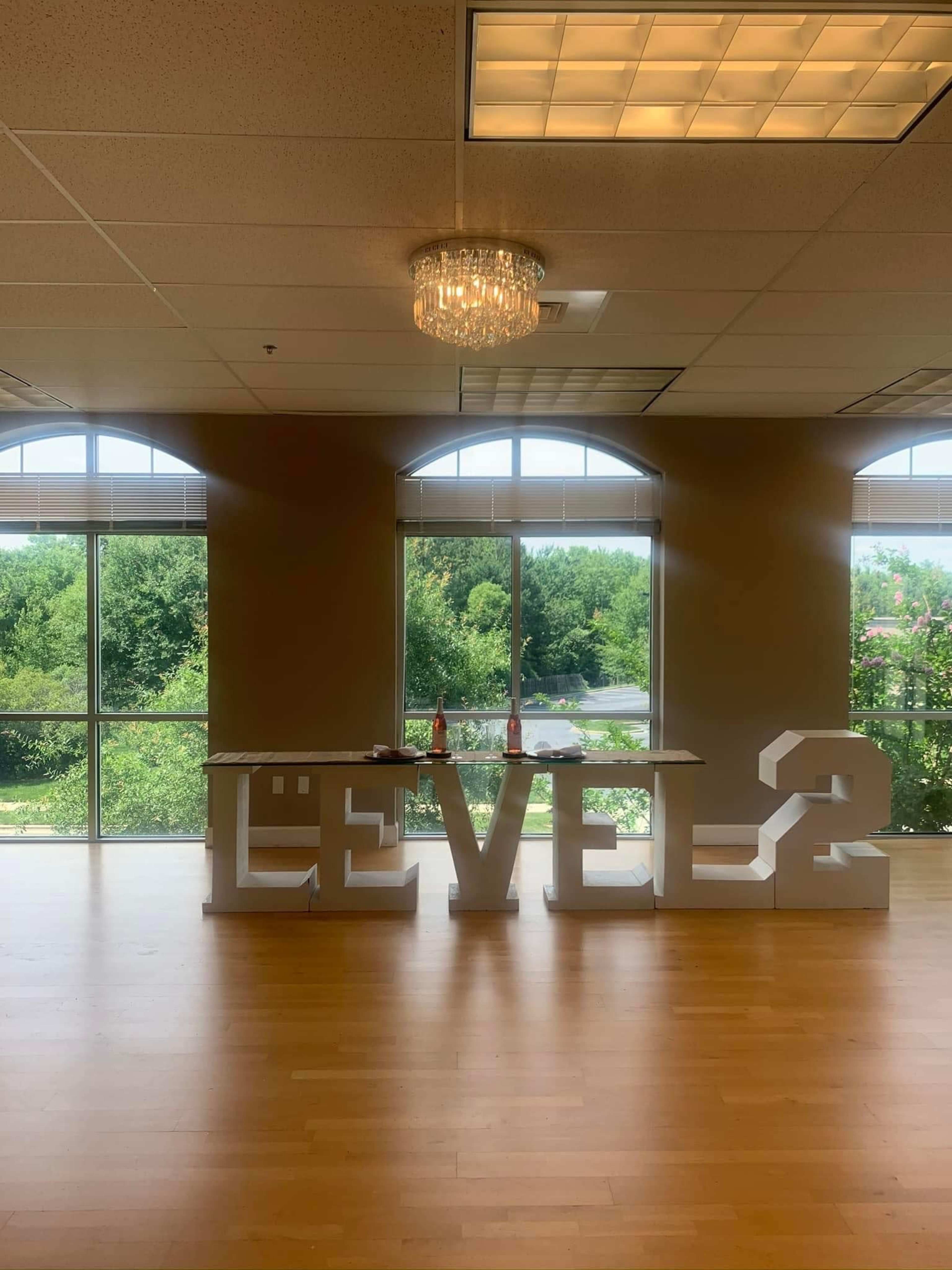 A spacious room with large windows, featuring a decorative chandelier and large white letters spelling "LEVEL 2" on the floor.