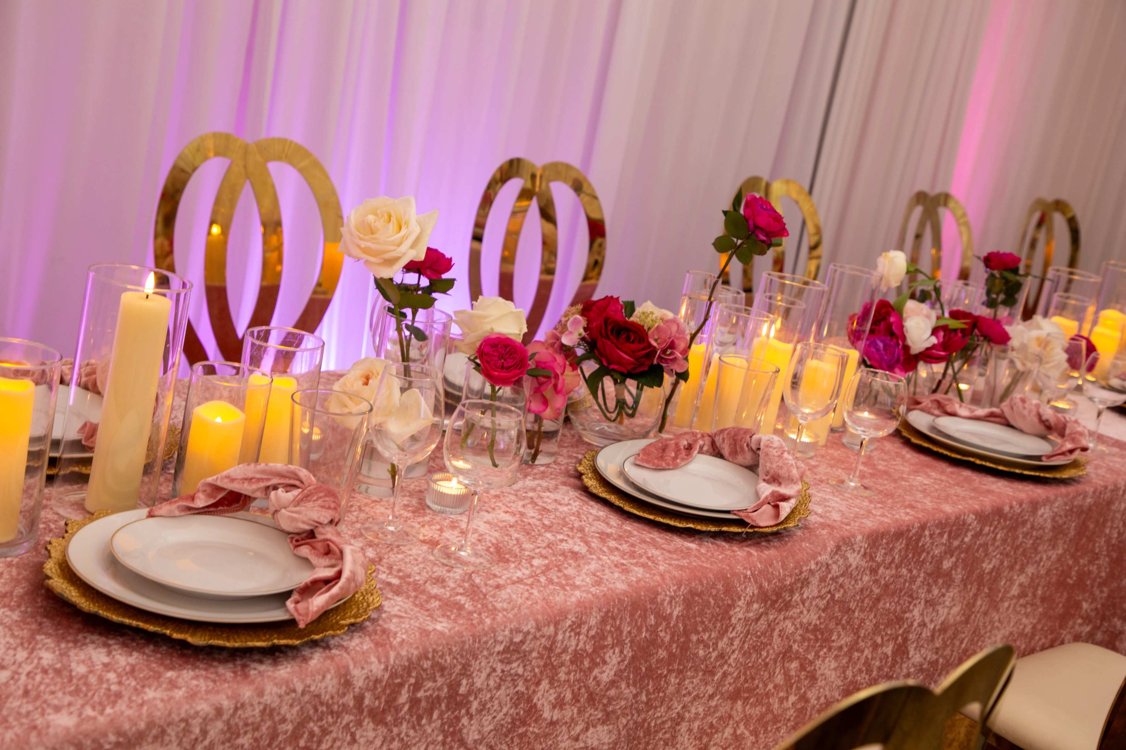 A elegantly set dining table features golden chairs, floral centerpieces, and candles in glass holders.