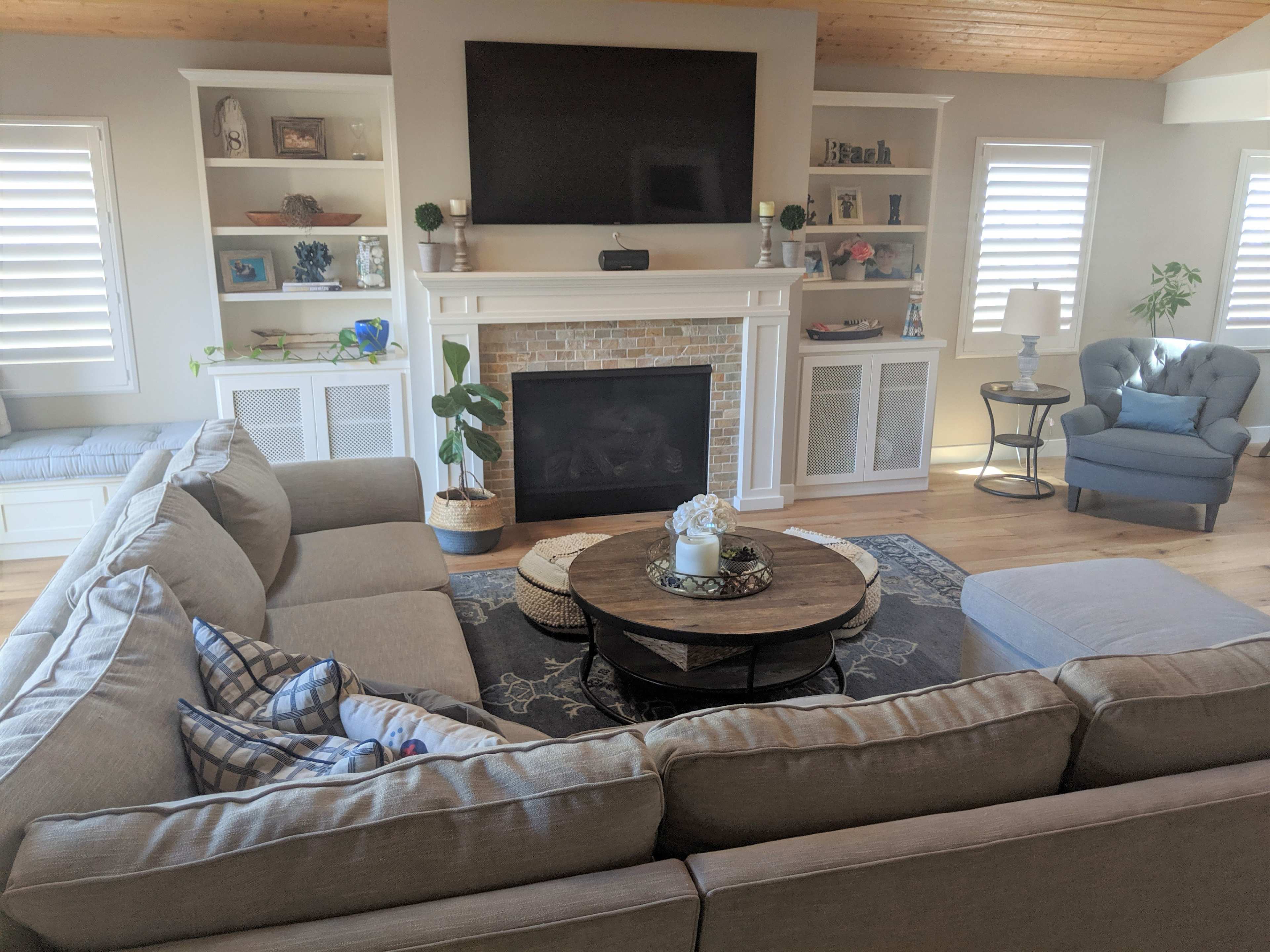 A cozy living room with a sectional sofa, a round coffee table, a brick fireplace, and various decorative items on the shelves.