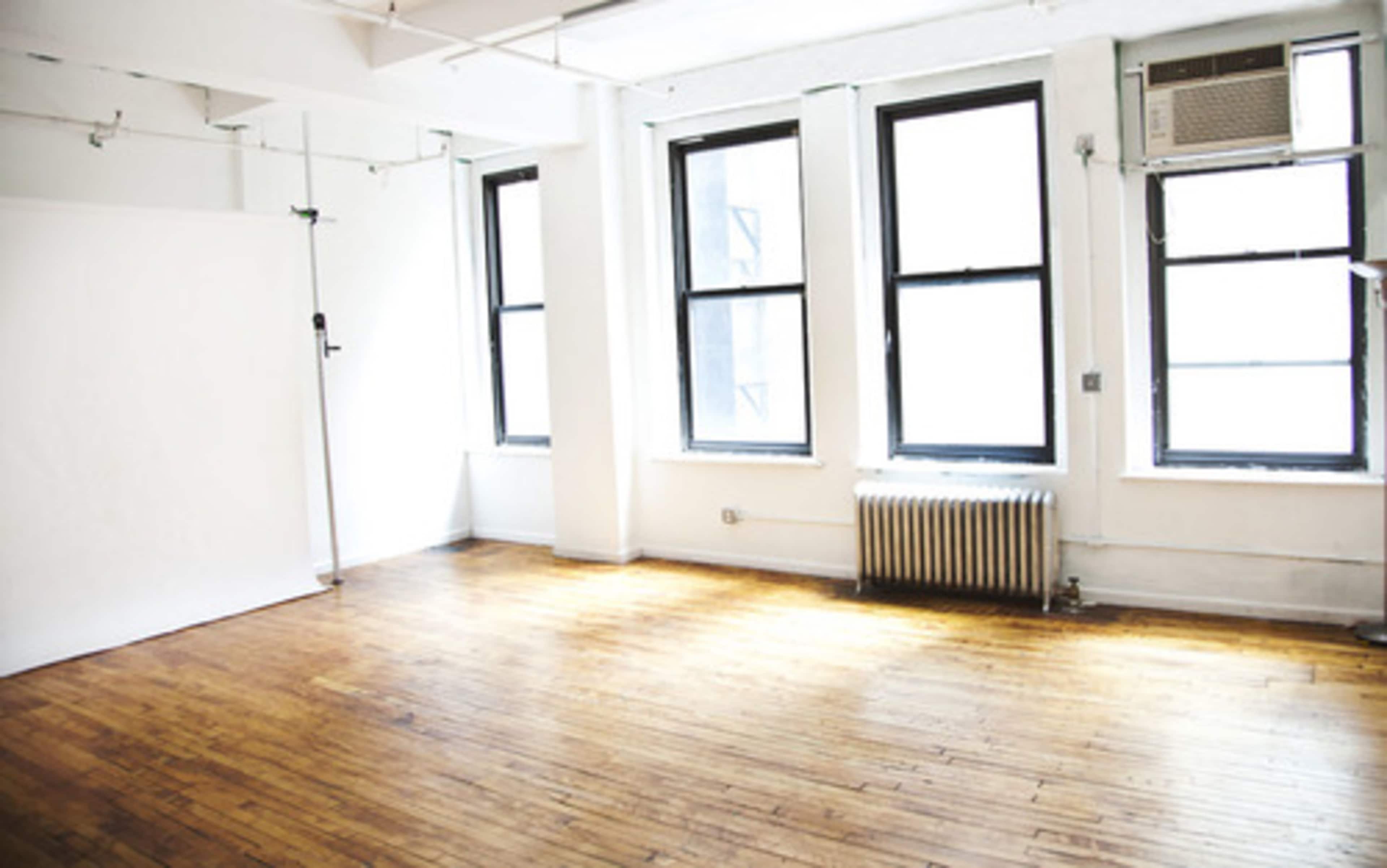 A bright, empty room with hardwood floors, large windows, and an air conditioning unit.