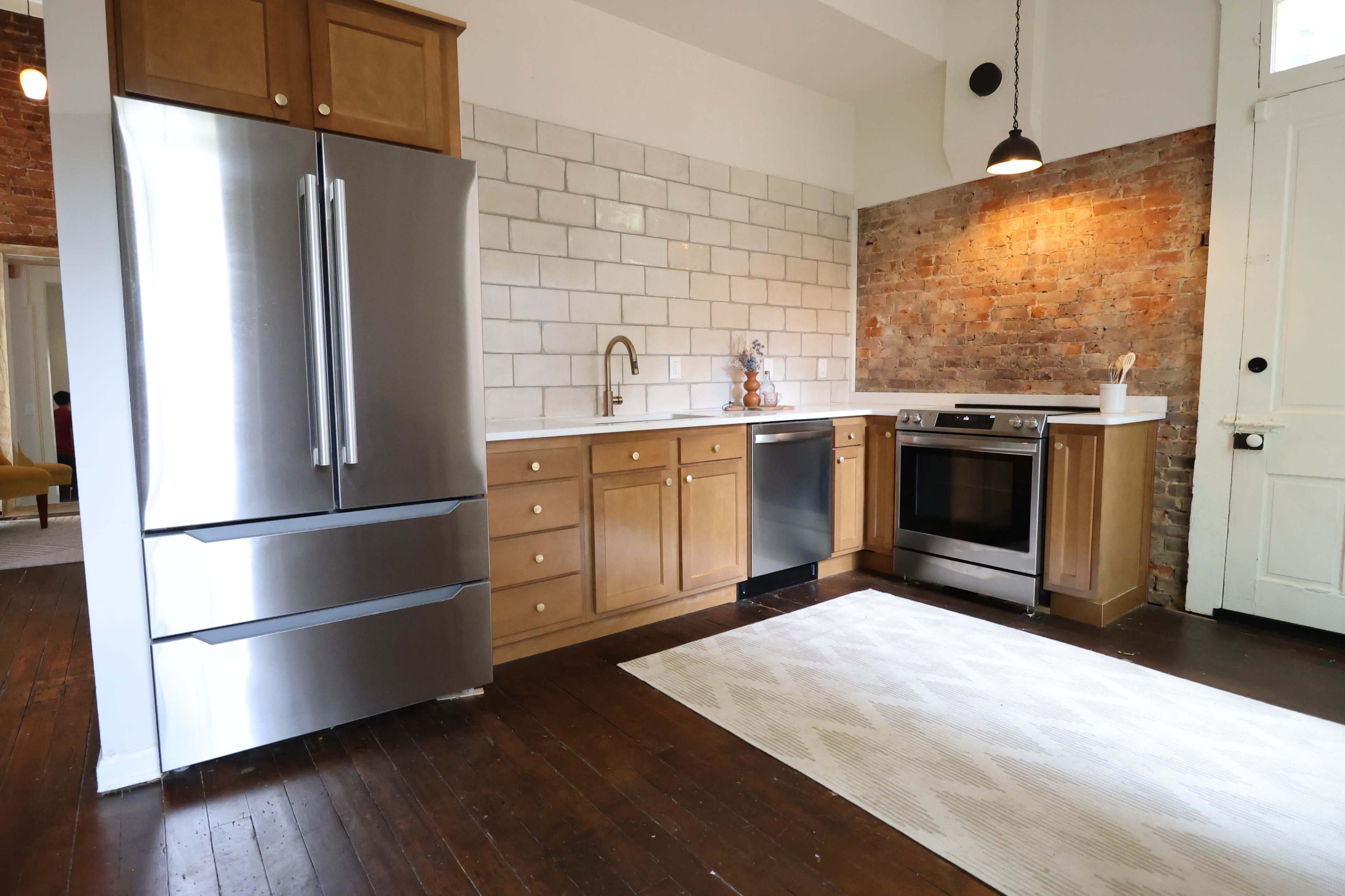 A modern kitchen featuring stainless steel appliances, wooden cabinetry, and exposed brick walls.