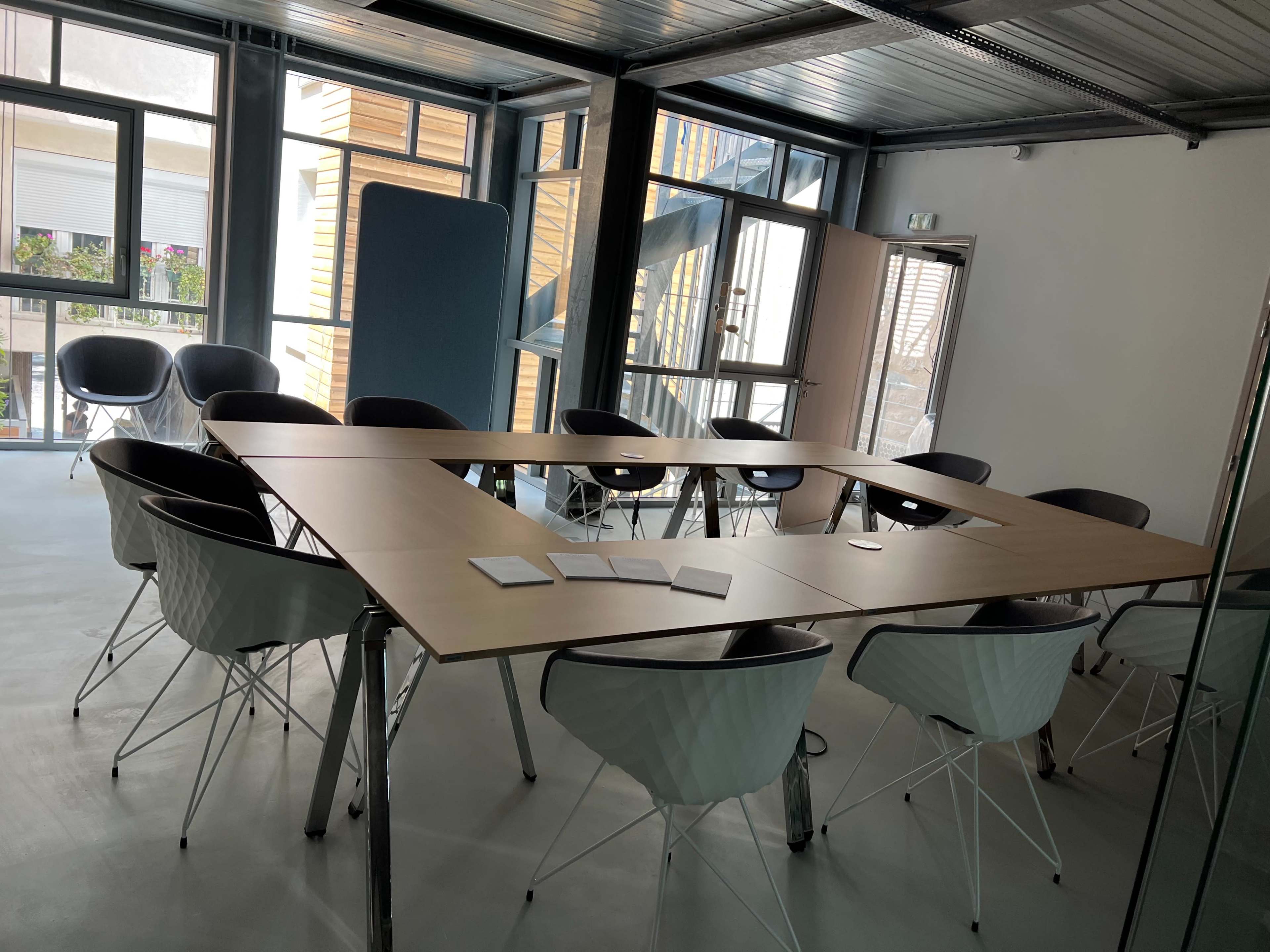 A large, modern conference room features a wooden table surrounded by white and black chairs, with windows letting in natural light.