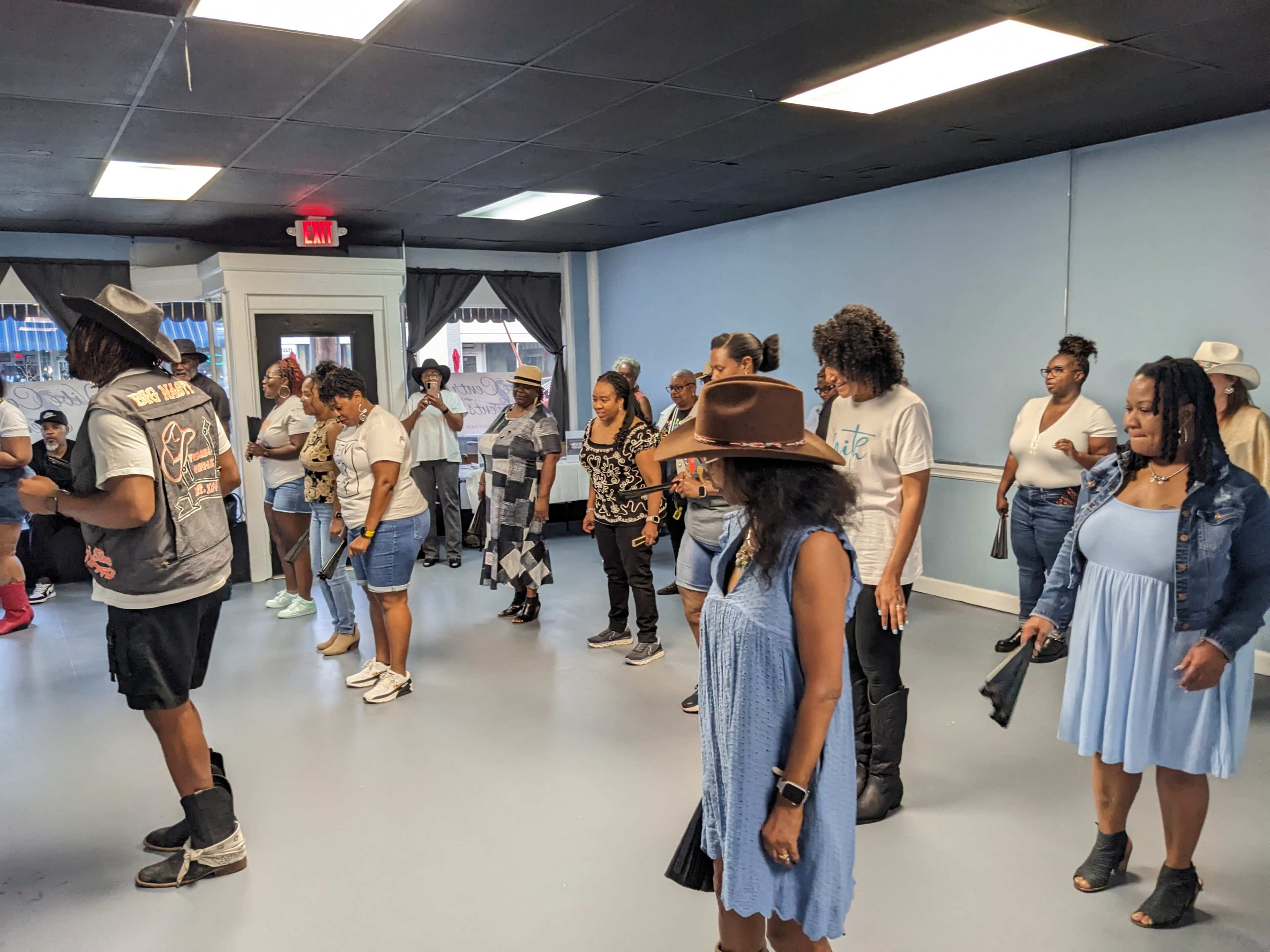 A group of people stands in a dance studio, participating in a line dance class.