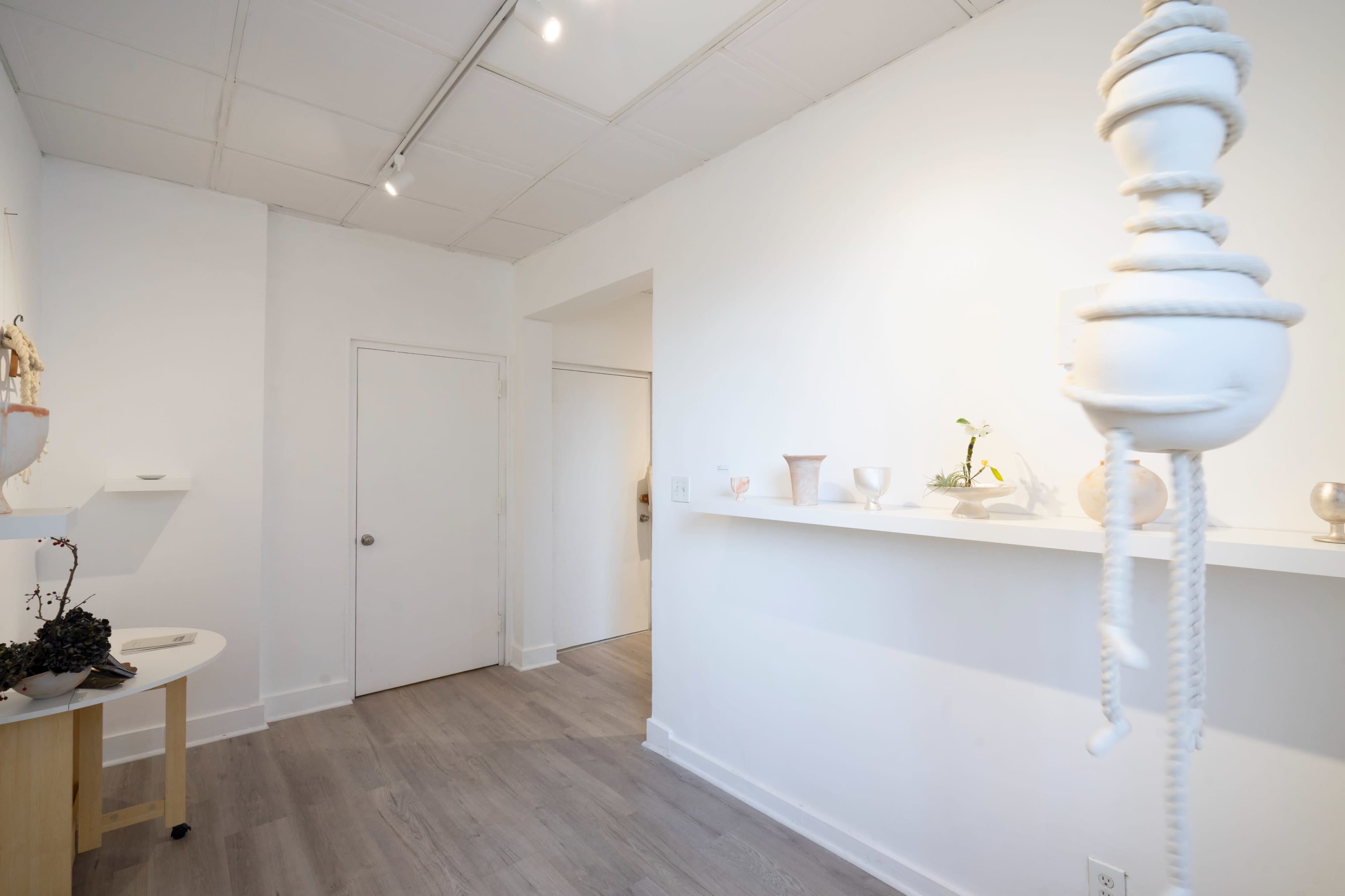 The image shows a minimalist interior space featuring a light-colored wall shelf with various decorative objects and a door leading to another room.