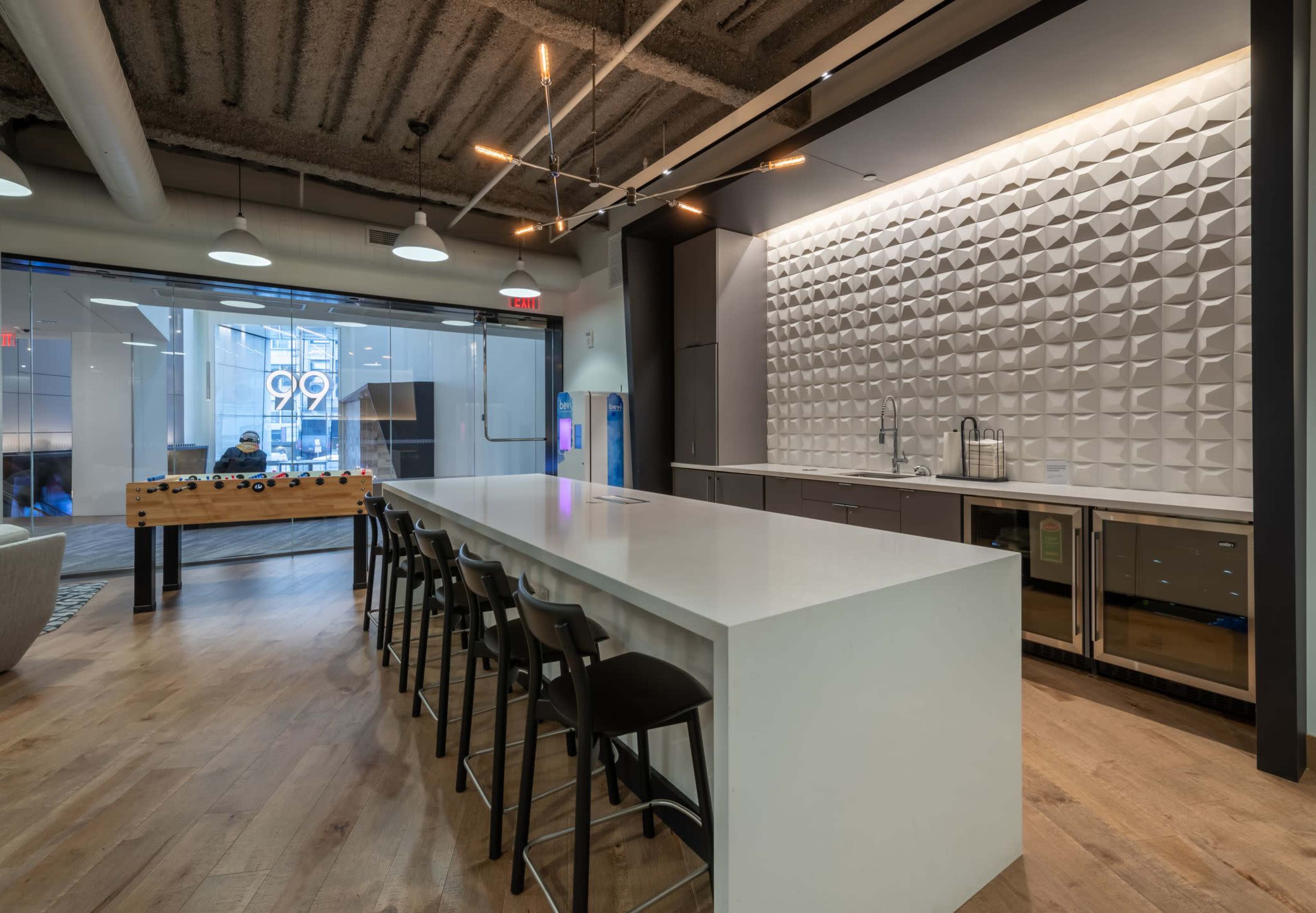 The image shows a modern kitchen space featuring a large white island, a textured backsplash, metal cabinets, and floor-to-ceiling windows.