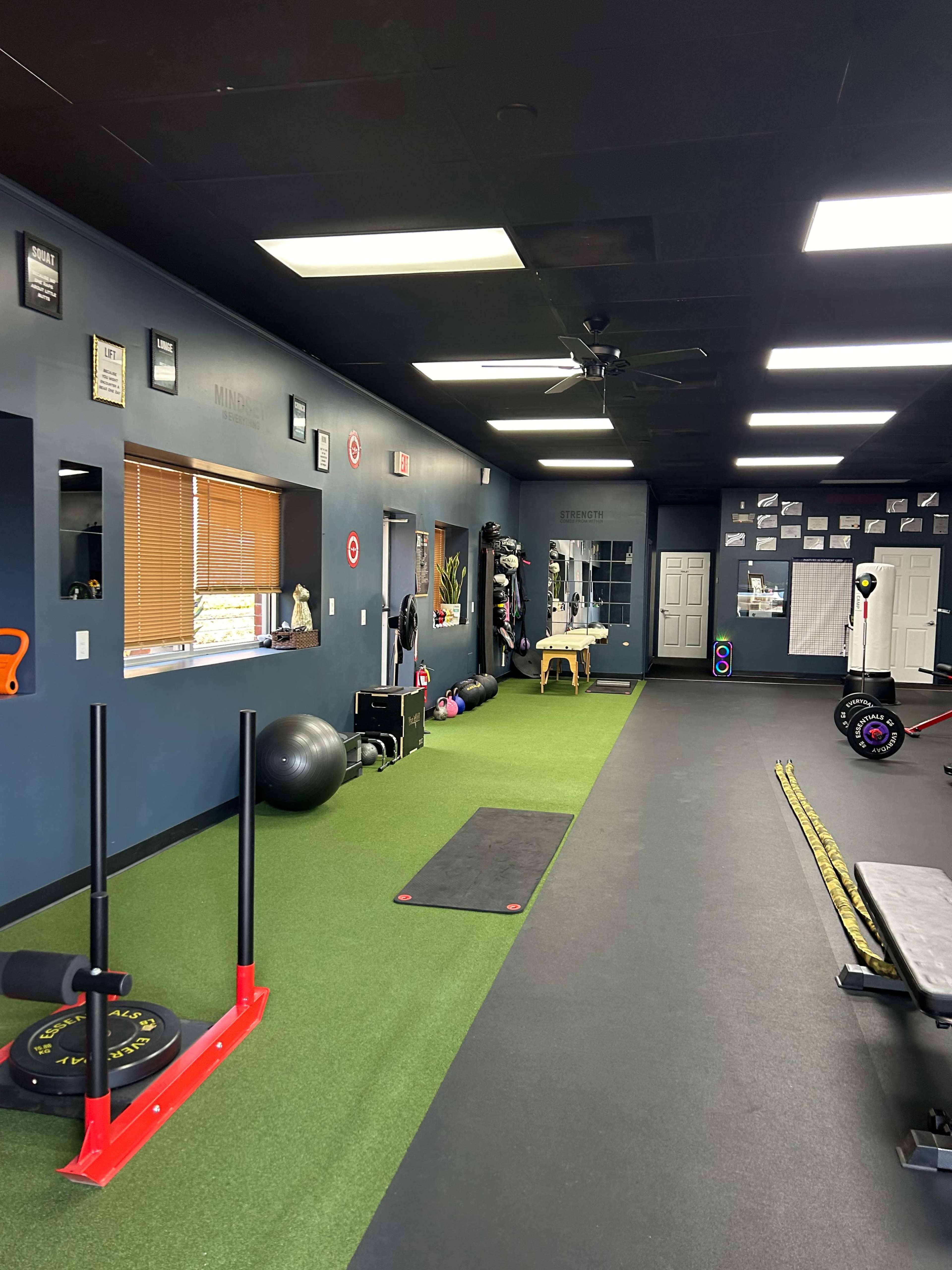 A fitness area featuring artificial turf flooring, exercise equipment, and a wall adorned with framed certificates and exercise-related items.