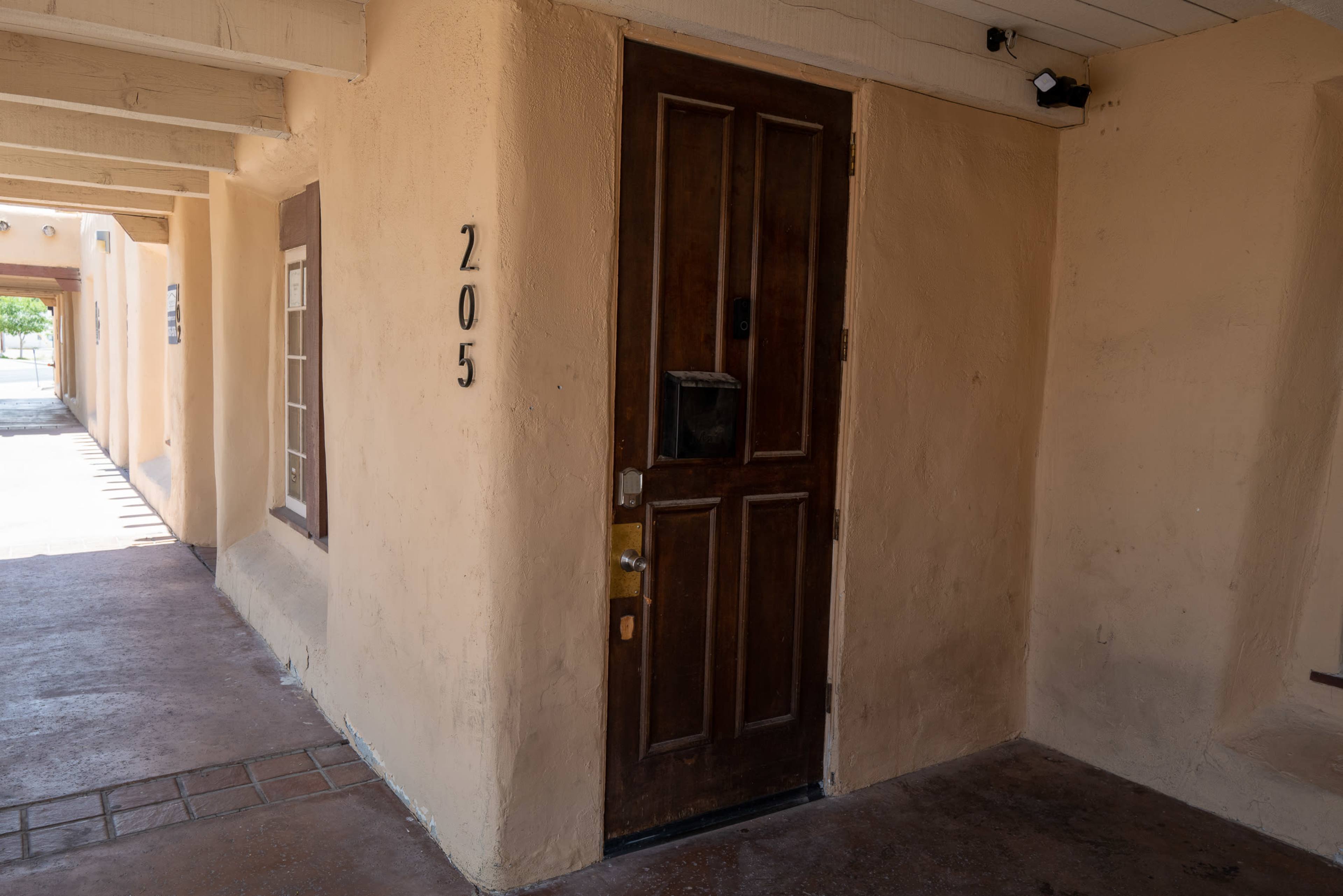 A wooden door marked "205" with a small window, situated in a stucco wall of a building.