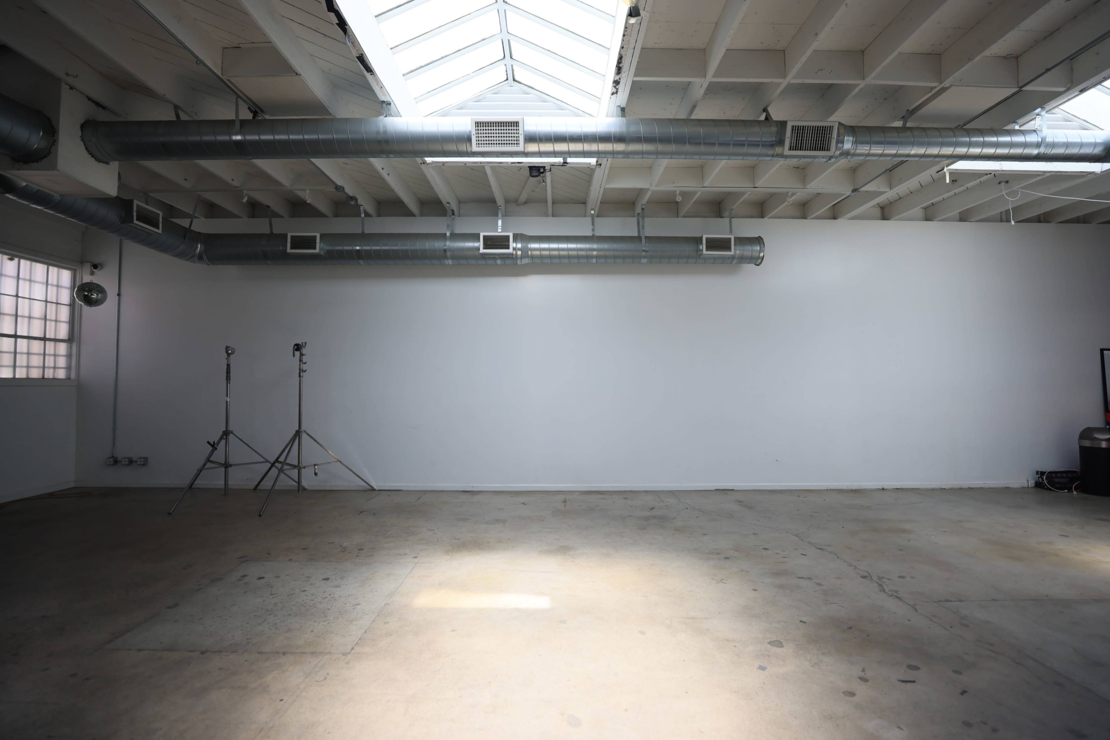 An empty room with a concrete floor, white walls, and a skylight, featuring metal ductwork along the ceiling.