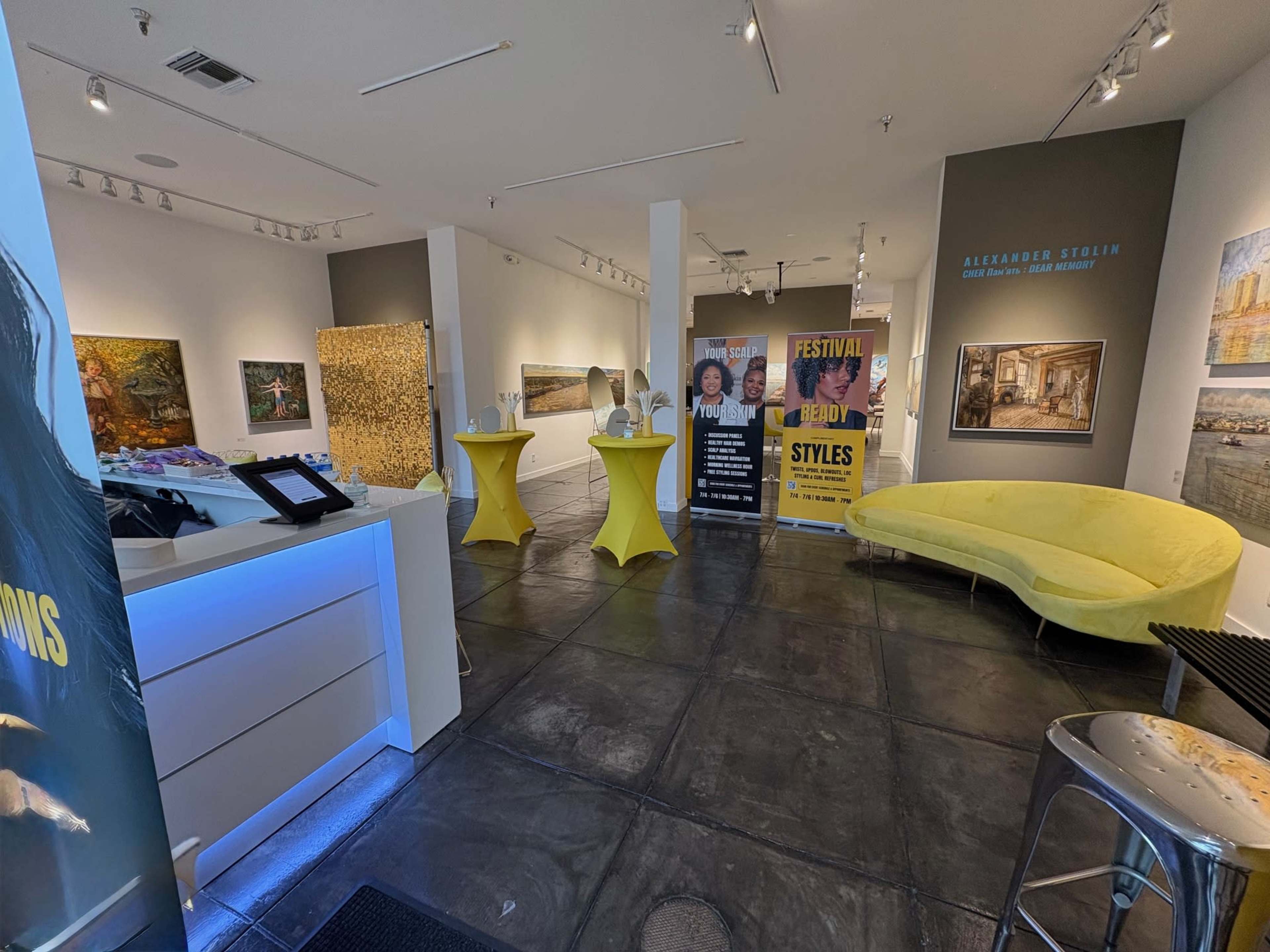 The image shows an art gallery interior featuring various artworks, two banners, and a lounge area with yellow furniture.