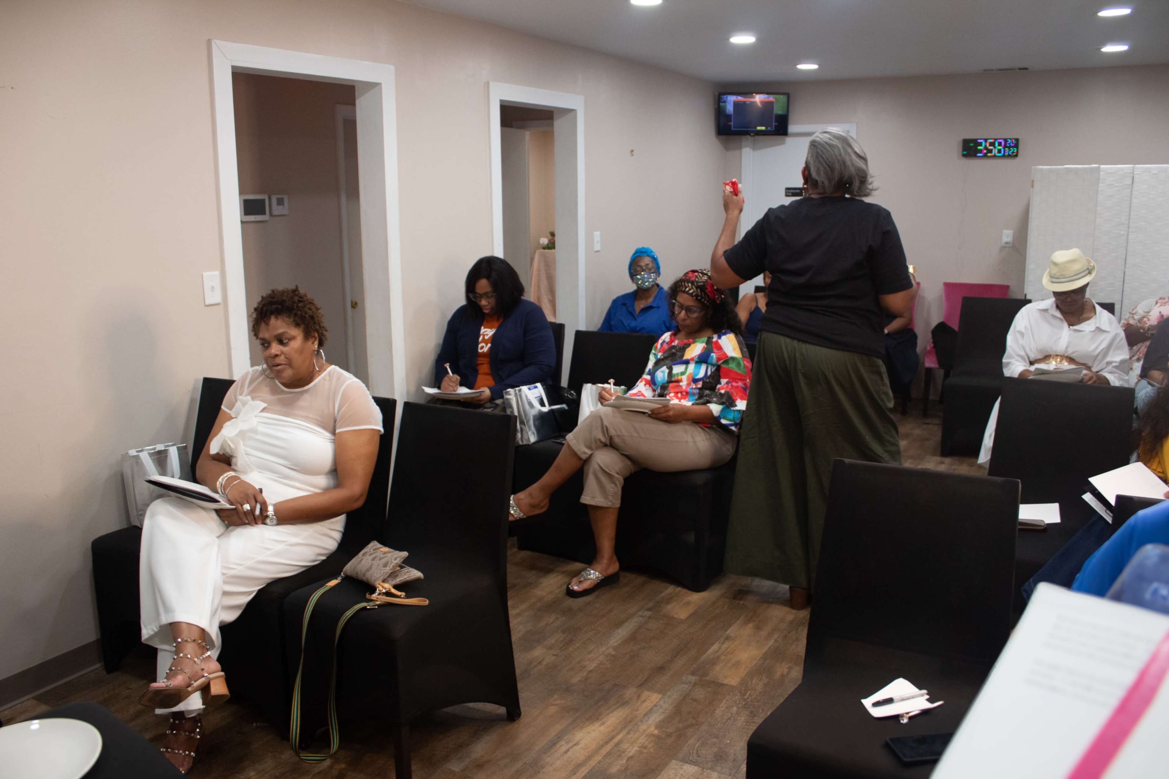 A group of people sits in a room, some taking notes while others appear to engage in discussion.