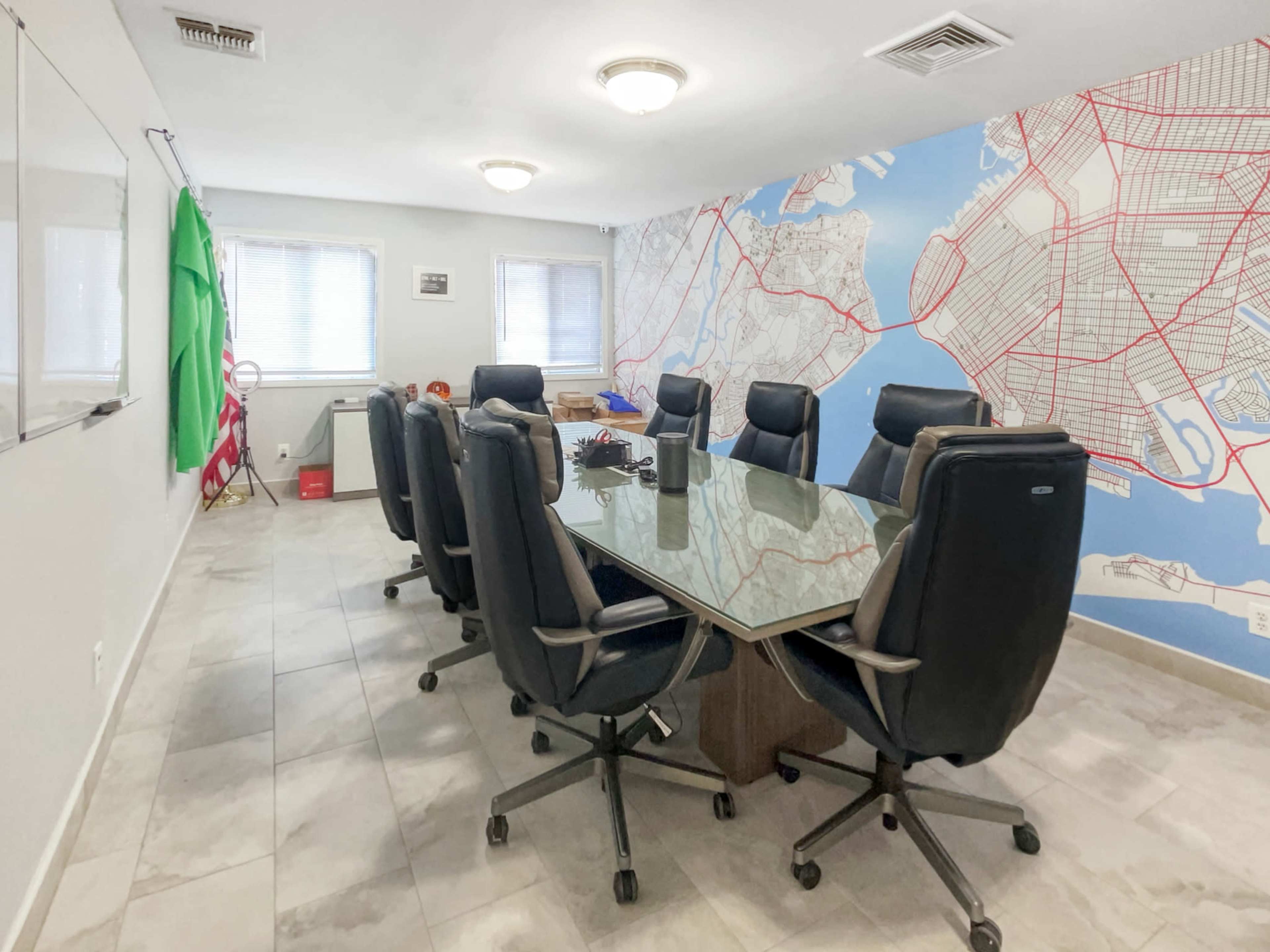 A conference room with a large glass table surrounded by black office chairs, set against a wall featuring a map design.