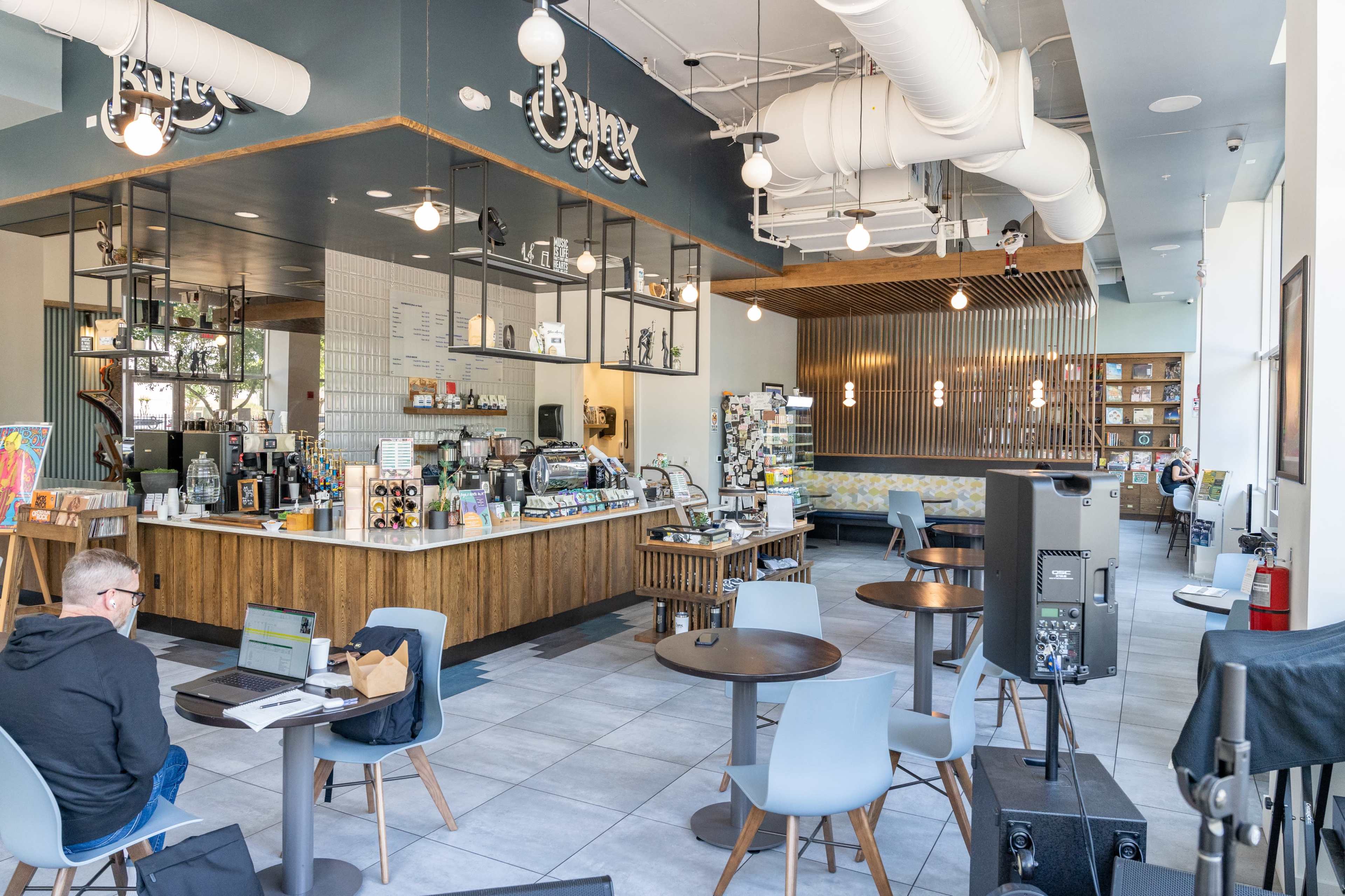 A modern café interior with a counter displaying various drinks and snacks, surrounded by tables and chairs for customers.