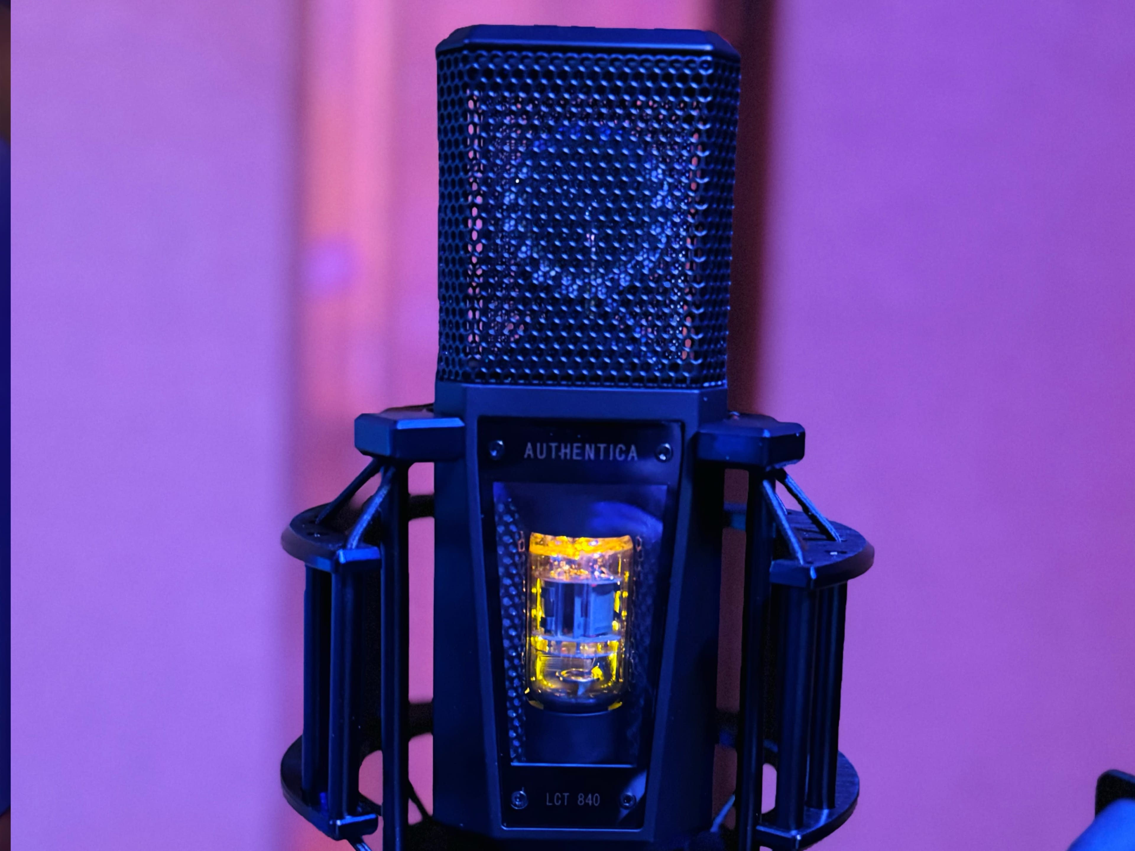 A black microphone with a mesh grille and a yellow light is positioned against a purple backdrop.